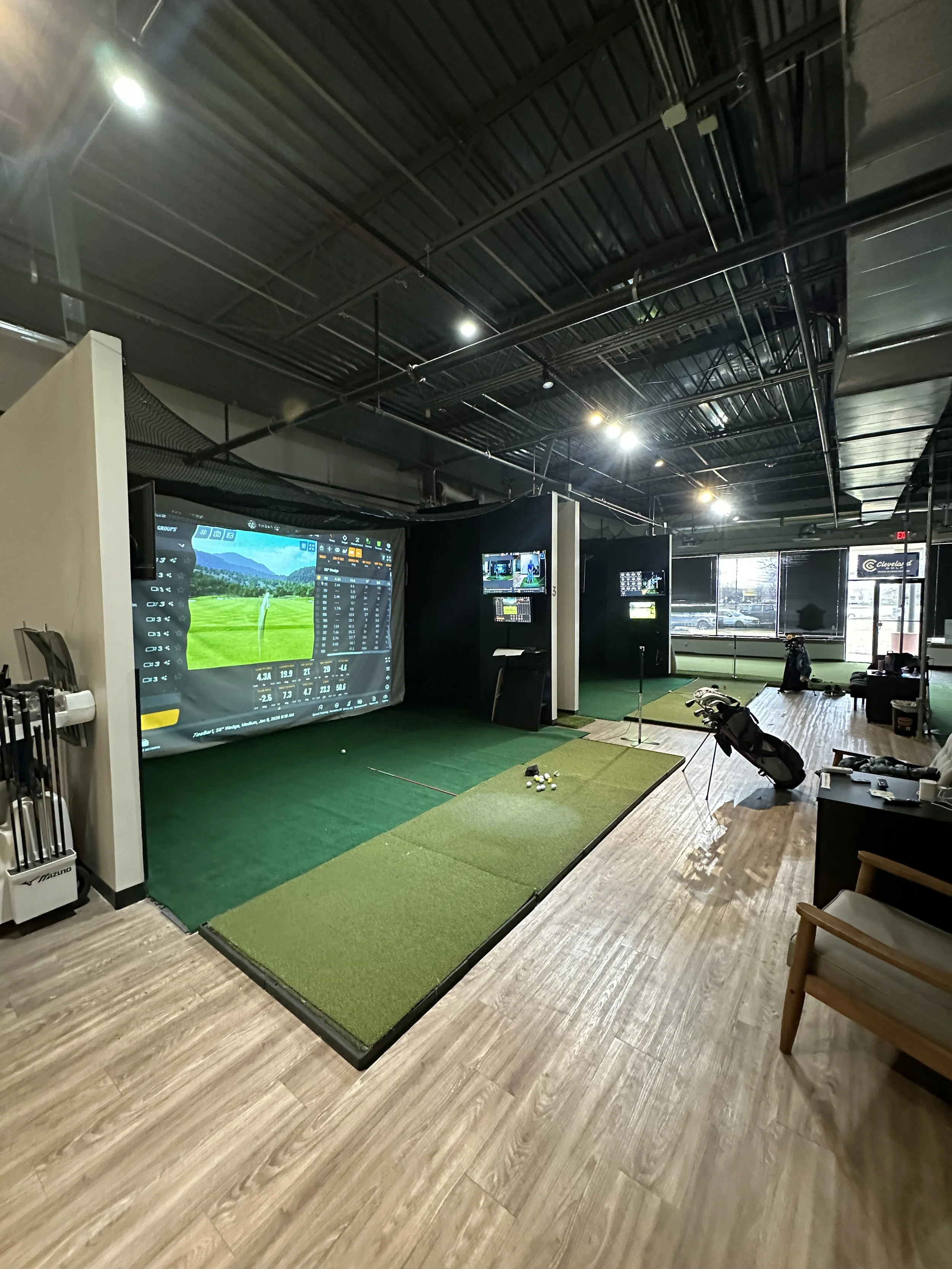 indoor golf simulator with wood floor and golf mats, large screens, high ceilings, and inviting lighting