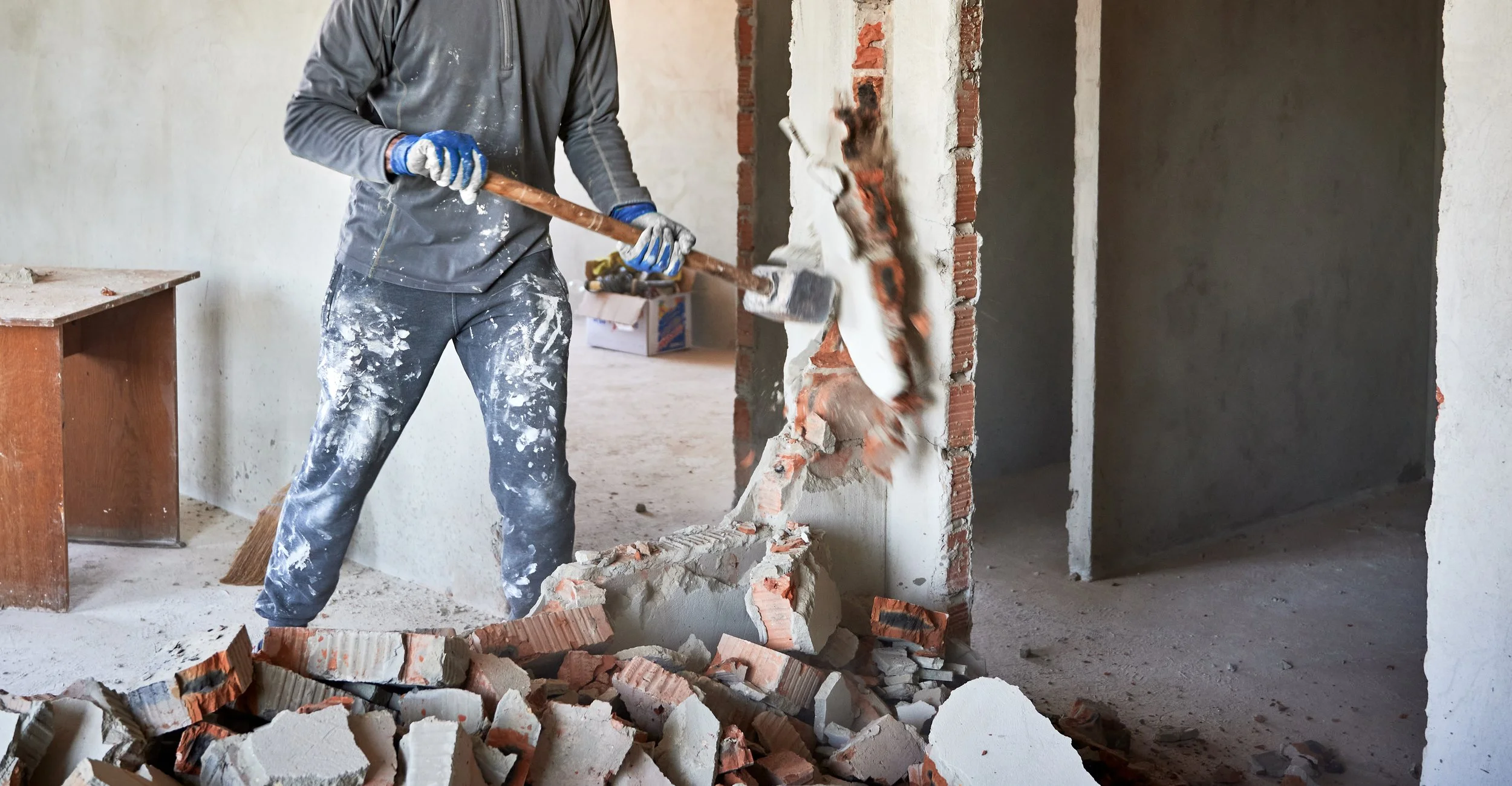 worker with sledgehammer, breaking down interior brick wall