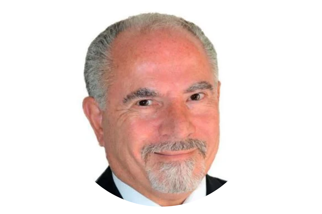 Portrait of an older man with gray hair, a beard, wearing a dark suit, white shirt, smiling.