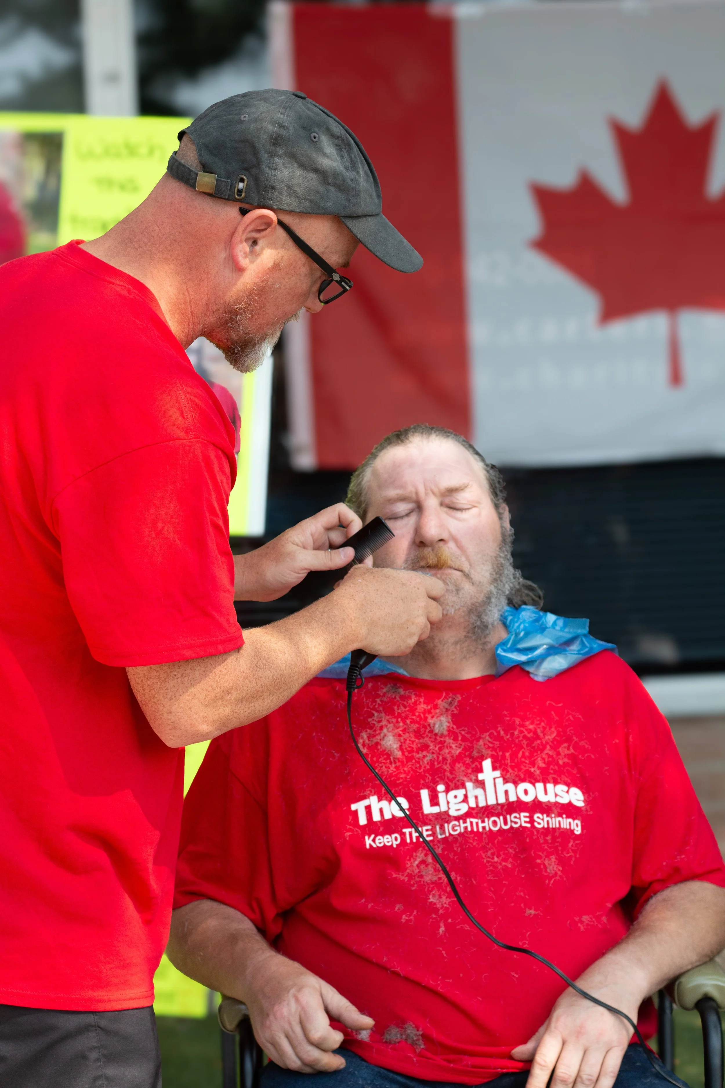 A man getting a shave at a public event, with an American flag in the background.