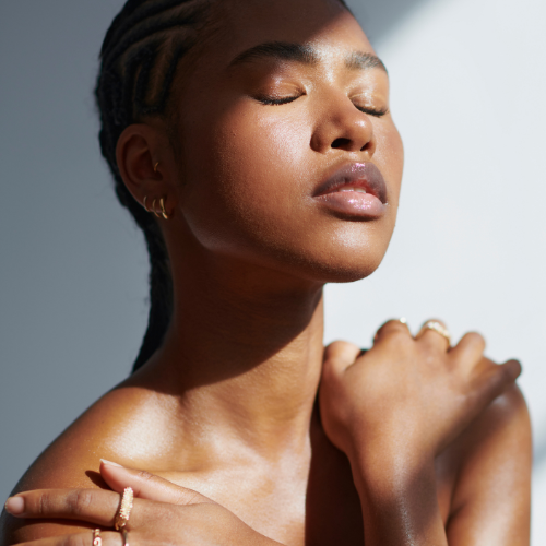 Close-up of a woman with closed eyes and relaxed expression, touching her shoulder in a well-lit setting.
