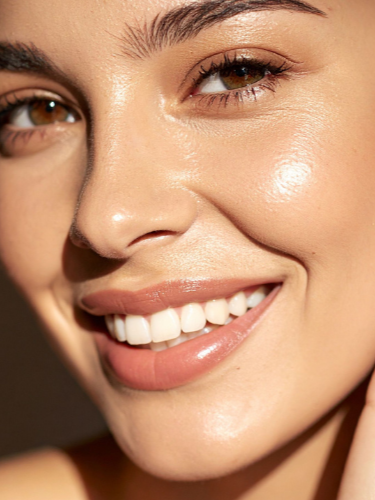 A close-up of a smiling woman with clear skin, full lips, and brown eyes.