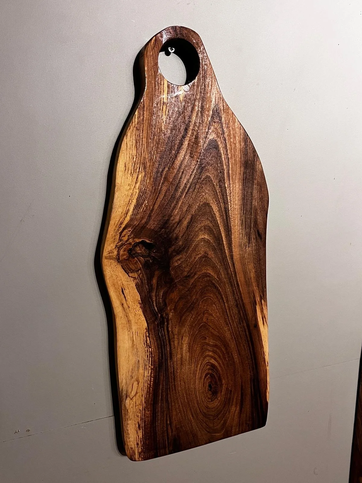 A wooden cutting board with a circular handle, made of dark and light wood with natural grain patterns.