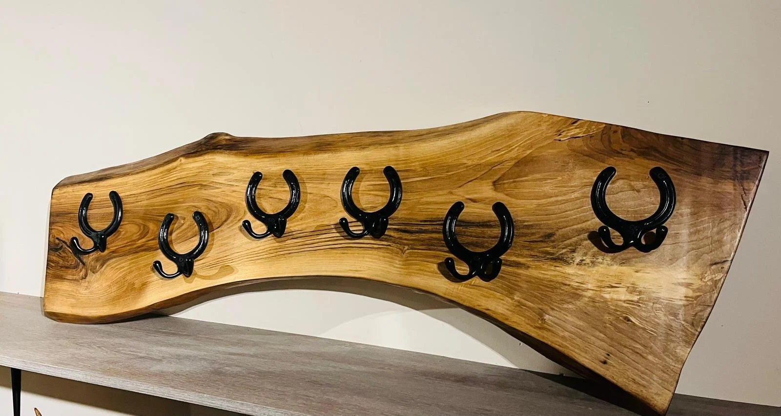 A wooden wall with six black hooks mounted on it.