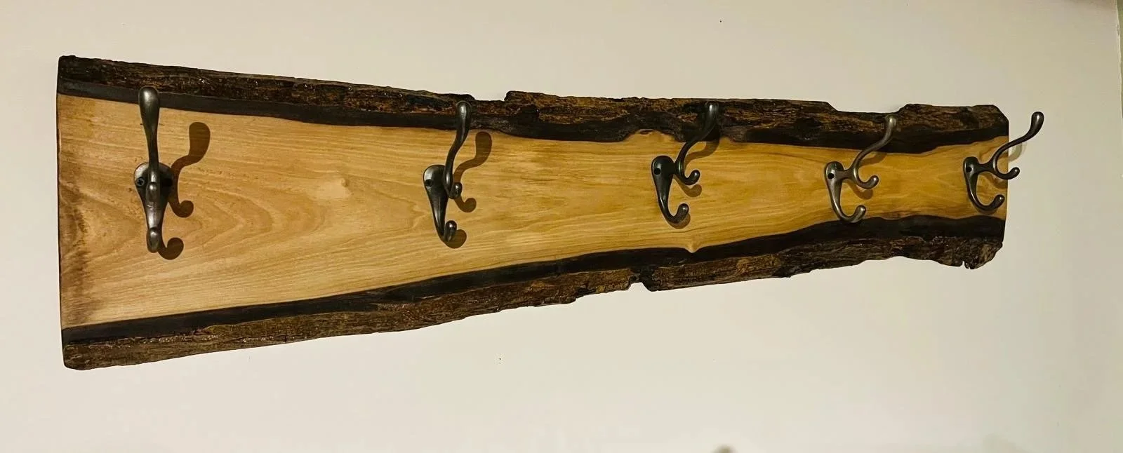 Wooden wall-mounted coat rack with metal hooks.