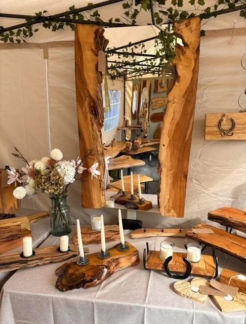 Display of handcrafted wooden home decor items, including a mirror, candle holders, and a flower arrangement, at a craft fair or market.