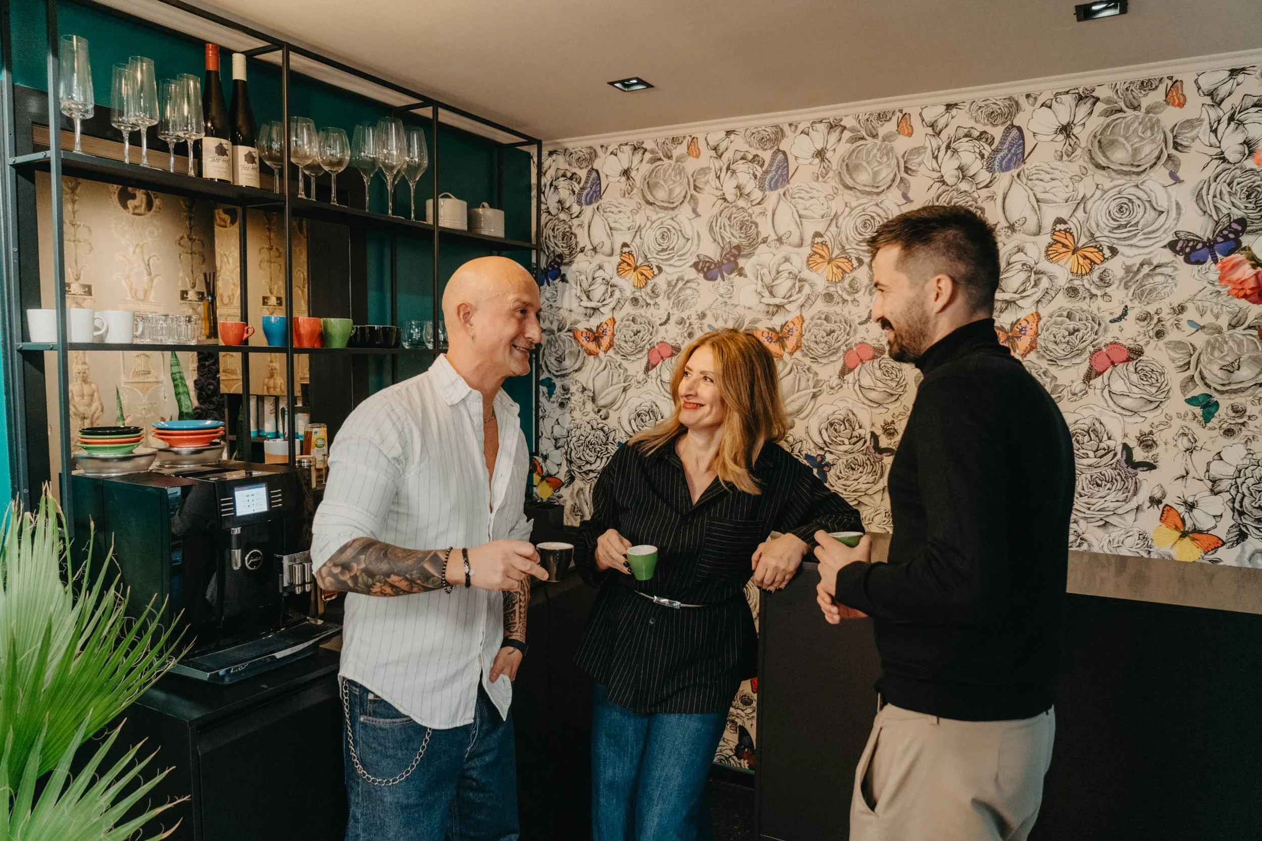 Drei Menschen trinken Kaffee, gut gelaunt und lachend, in einer stilvoll eingerichteten Küche