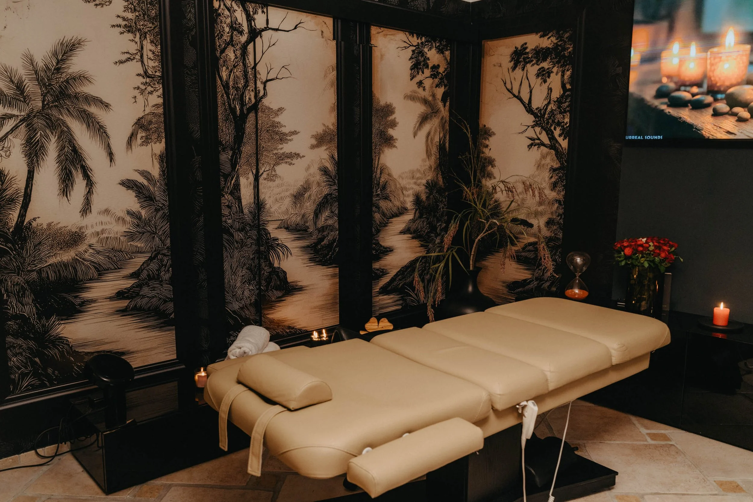 Behandlungsliege in einem Spa oder Massagezentrum, mit einer Wanddekoration im asiatischen Stil und Kerzen für eine entspannte Atmosphäre.