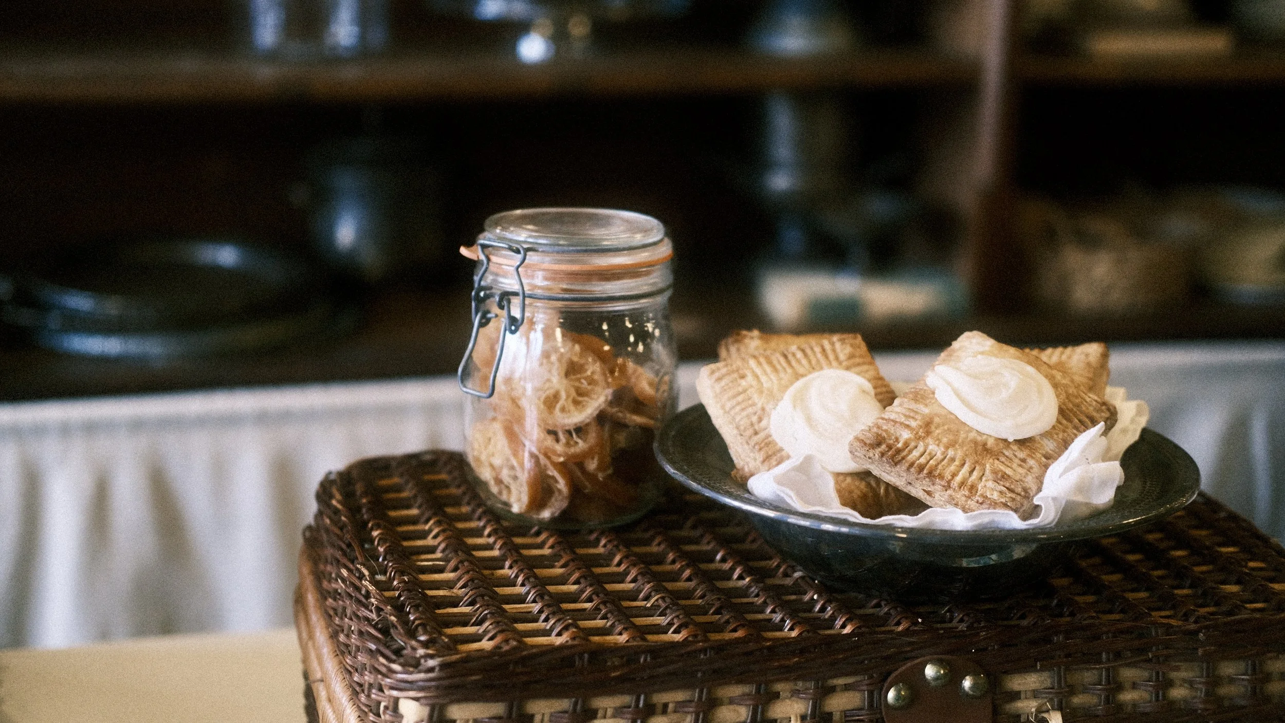 Plate of baked goods topped with cream and a jar of dried fruit on a woven table.