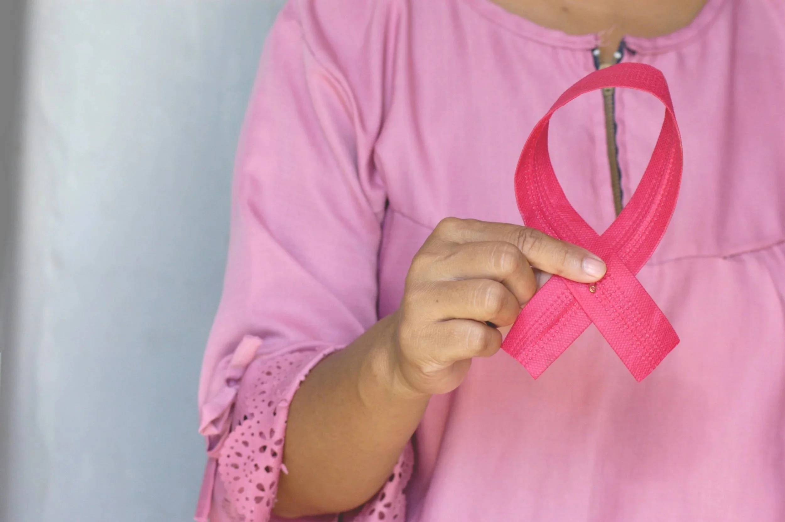 Close-up of a person wearing a pink shirt holding a pink ribbon, a symbol of breast cancer awareness.