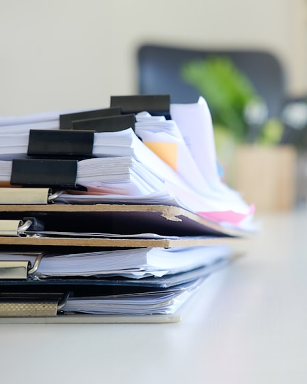 A stack of disorganized paperwork and folders on a desk in an office setting.