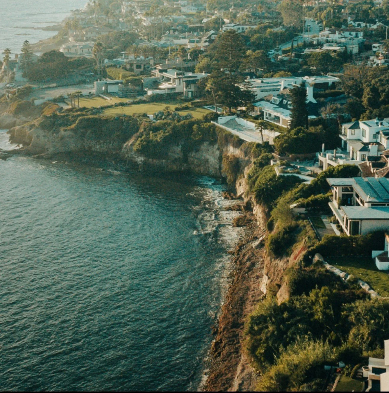 Aerial view of a coastal residential area with houses along a cliffside overlooking the ocean.