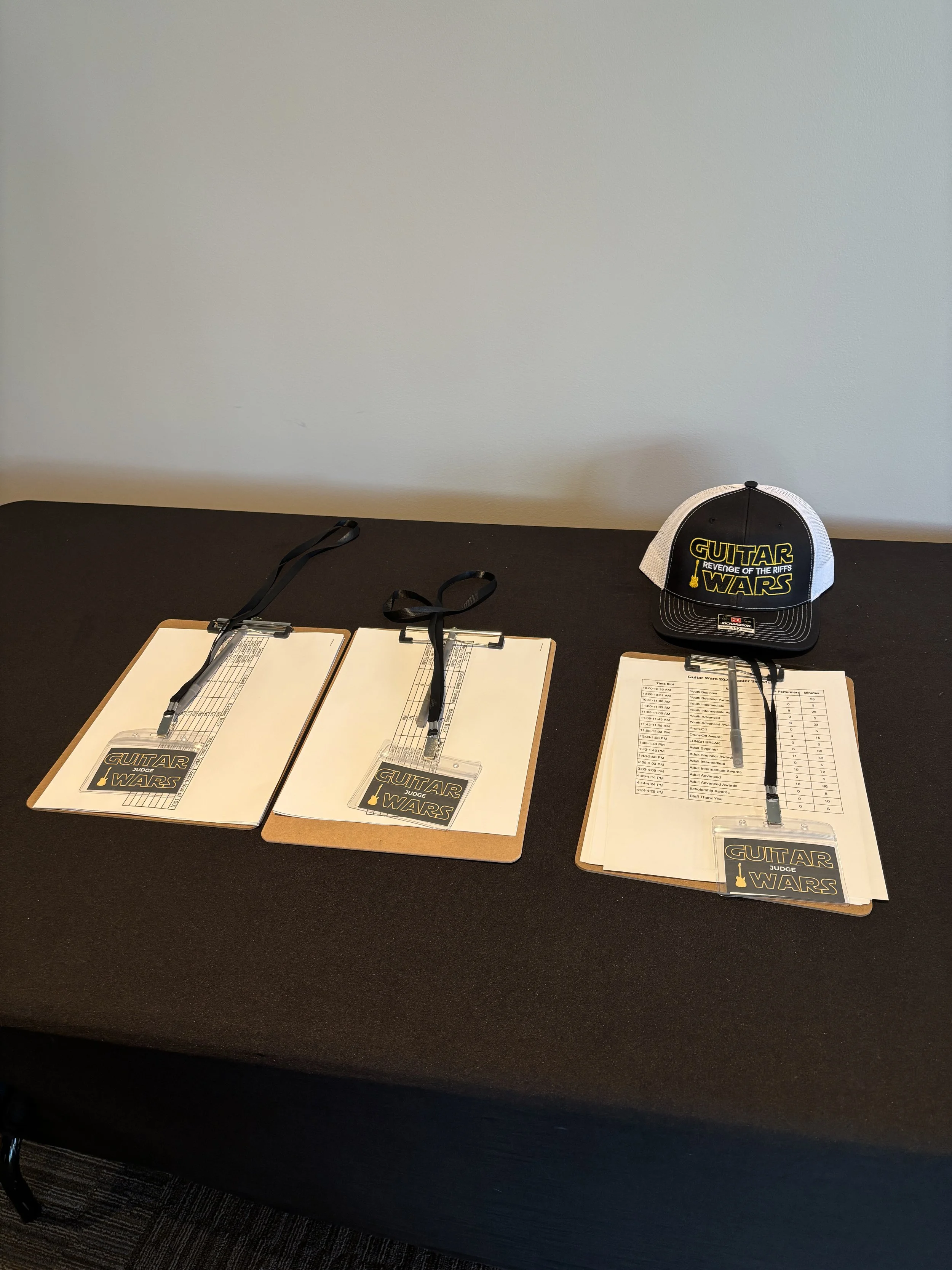 Guitar Wars judging sheets with lanyards and a hat on a black table