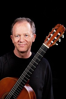 A man holding an acoustic guitar against a black background