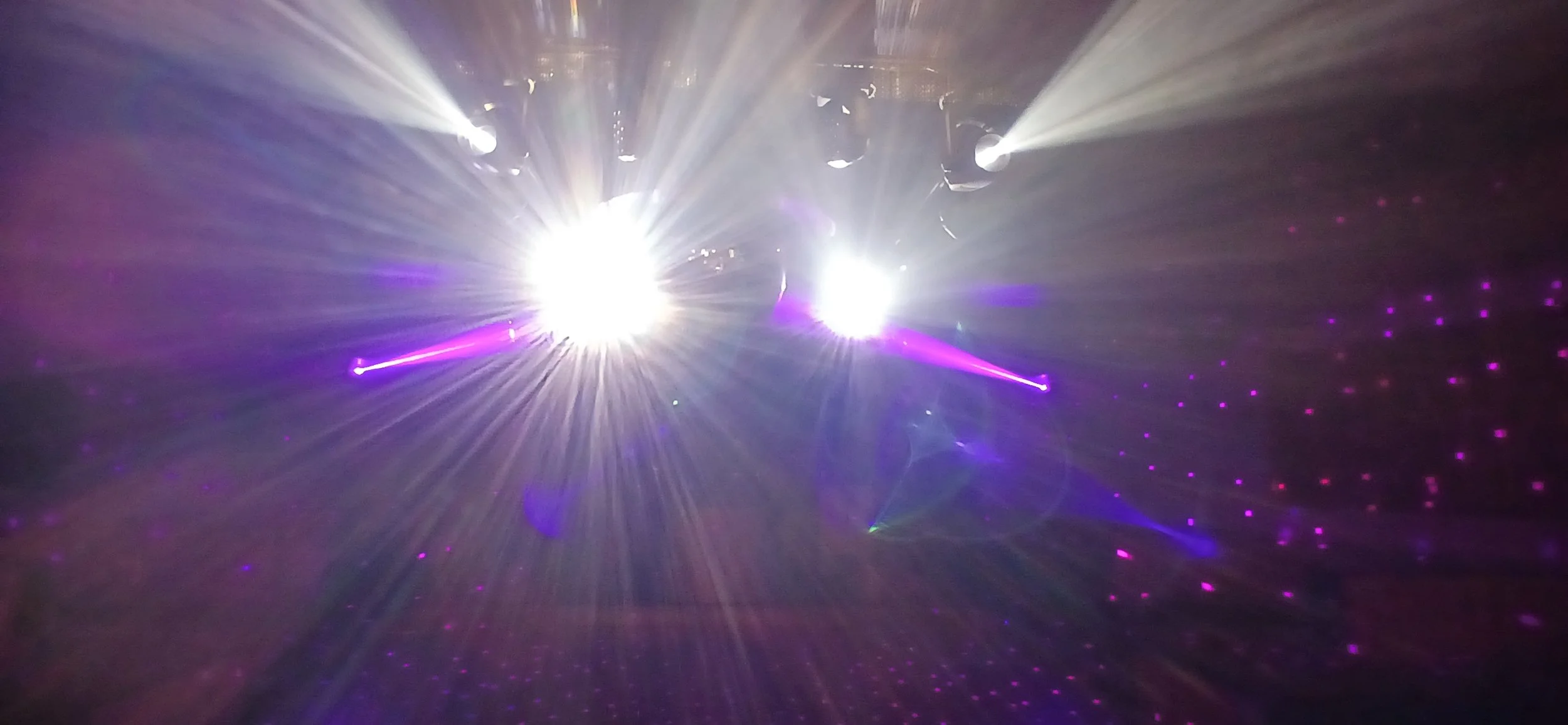 Bright white and purple laser lights projecting in a dark room with scattered purple dots of light.