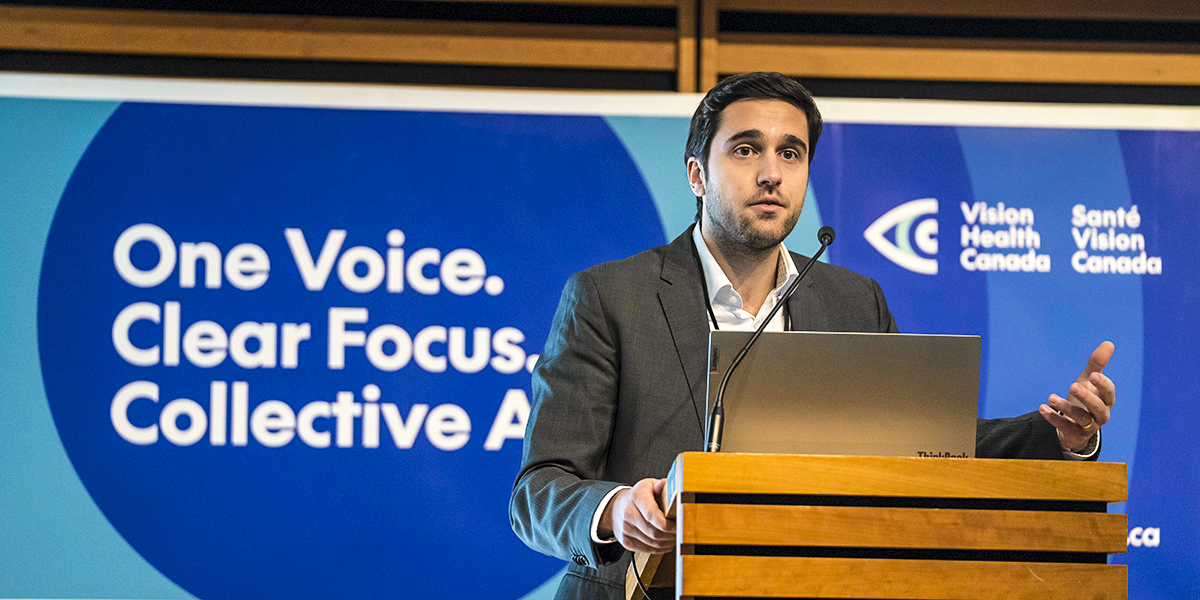 Dr. Marko Popovic of St. Michael's Hospital moderates a discussion from the podium. Seen in the background is a Vision Health Canada branded banner.