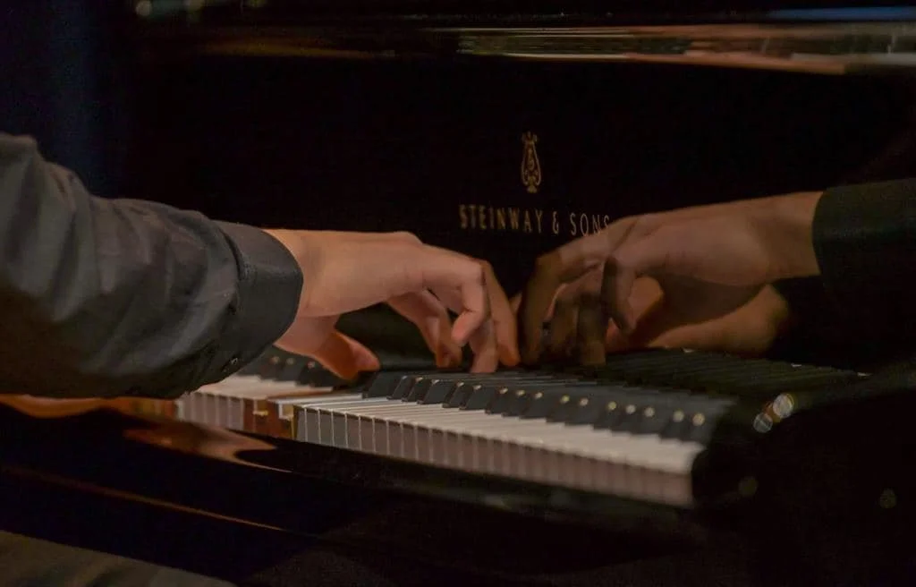Two people playing a Steinway & Sons grand piano together, with their hands on the keys.