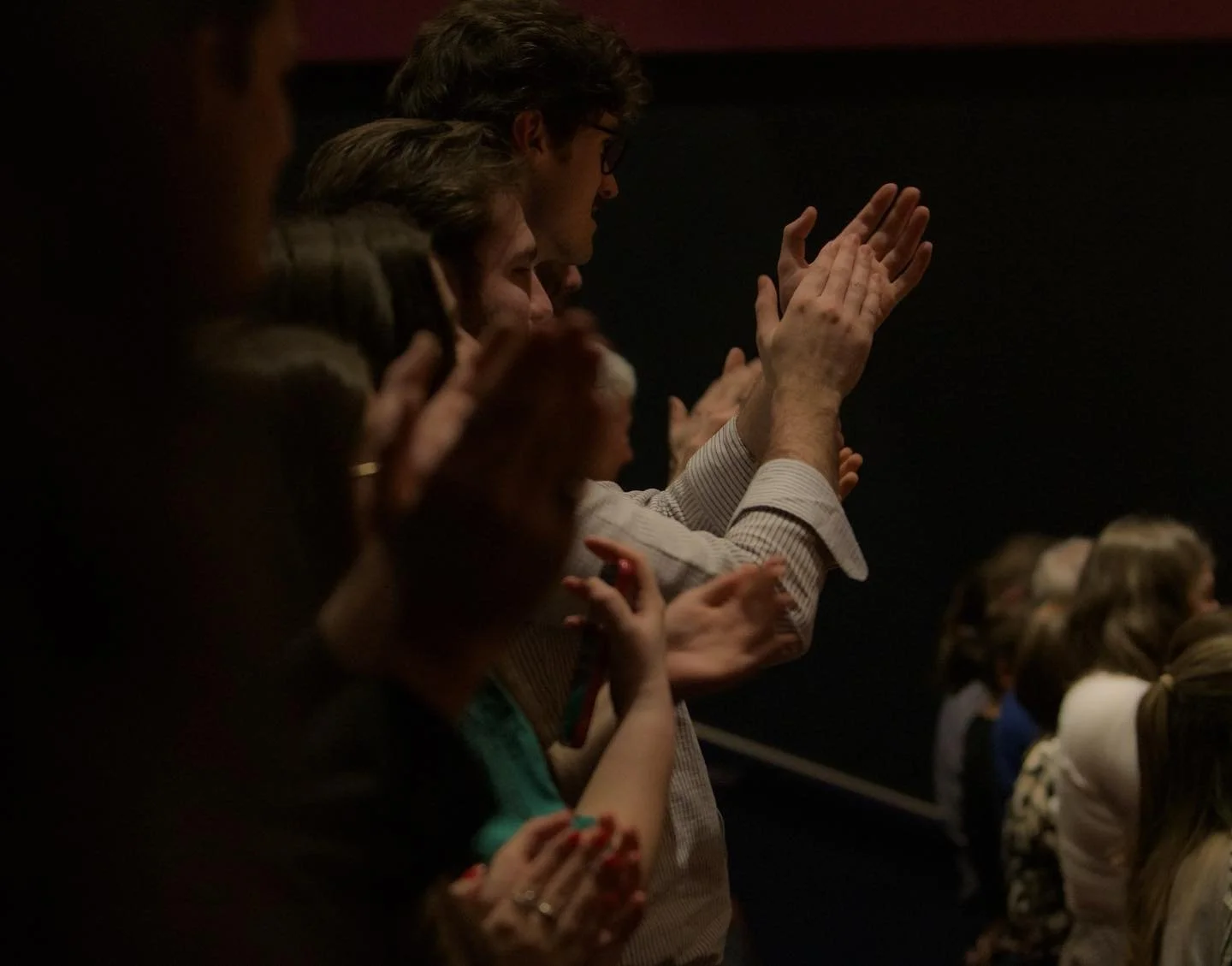 Audience members clapping and applauding inside a dark auditorium.