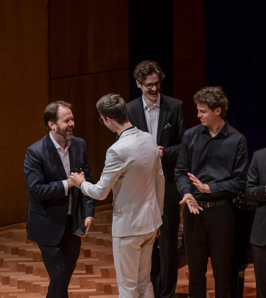 Group of men in formal attire smiling and shaking hands at an indoor event.