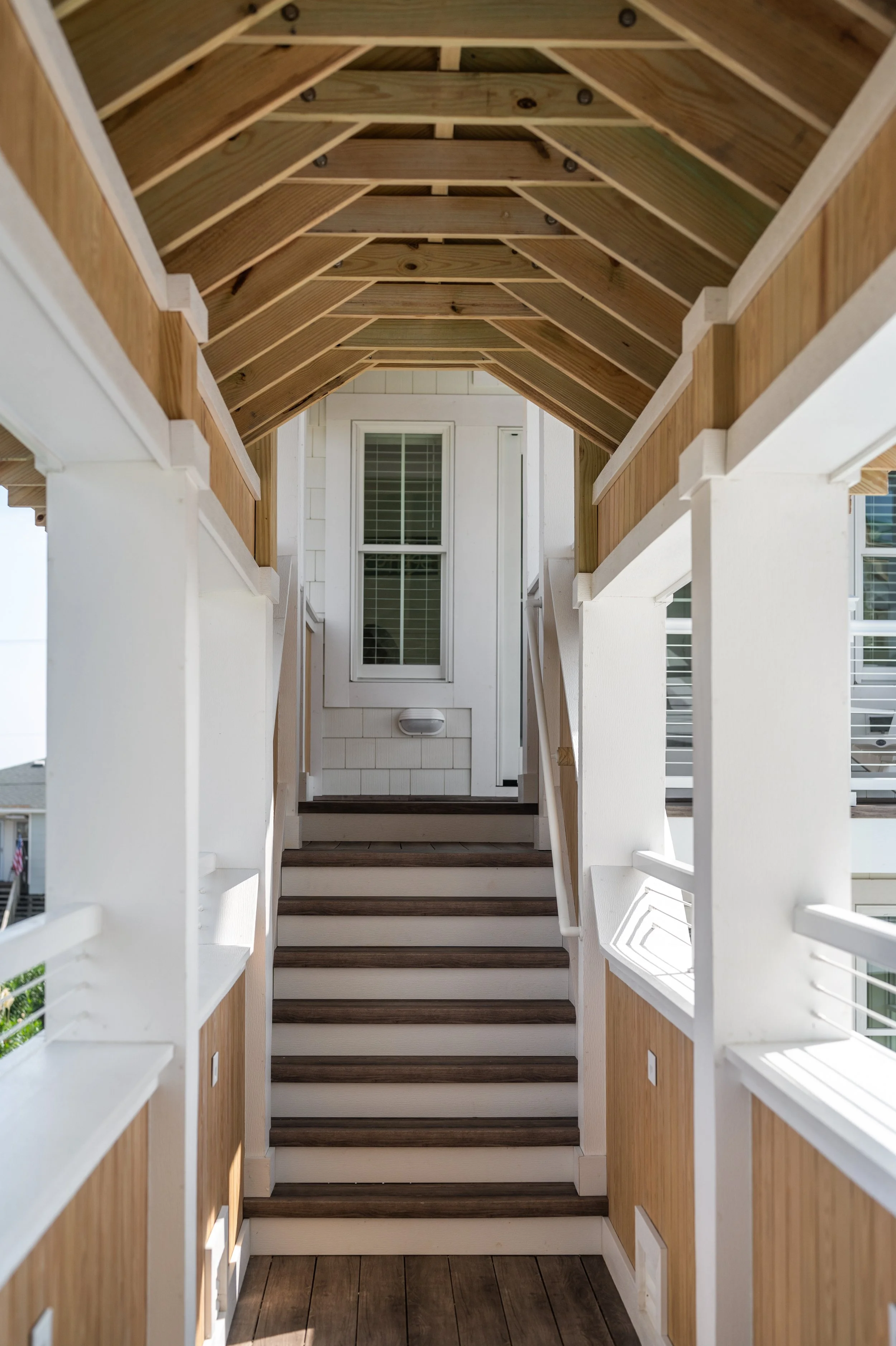 Wooden stairs leading up to a porch with white railings and a door with a window in a house exterior.