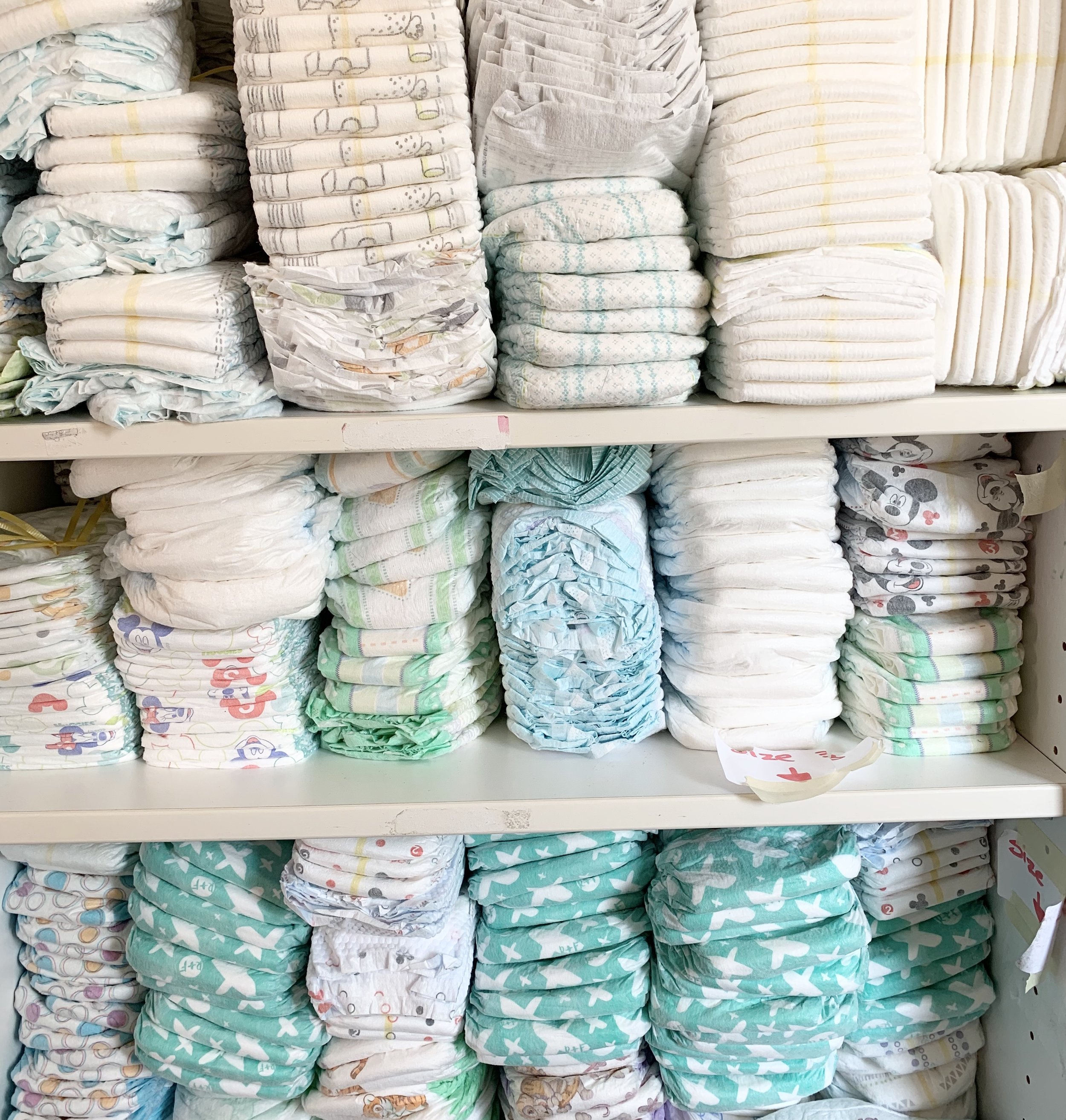 Shelves stocked with various stacks of disposable diapers in different colors and patterns.
