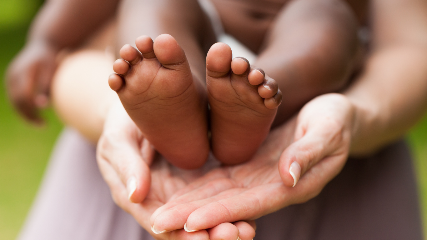 Close-up of an adult's hands holding a baby's feet outdoors.
