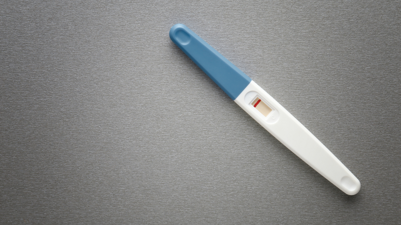 Pregnancy test with a single pink line indicating a negative result placed on a gray textured surface.