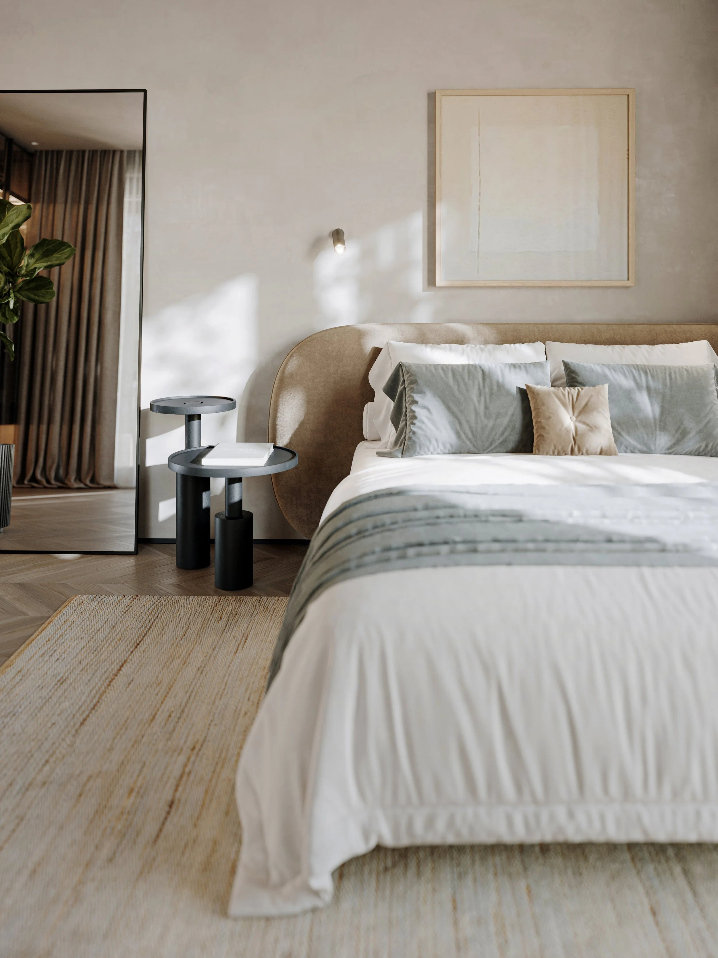 A modern bedroom with a beige upholstered headboard, white bedding with a grey and beige blanket, multiple grey and beige throw pillows, a nightstand with a book, a large mirror, a potted plant, abstract artwork on the wall, and sunlight streaming in.