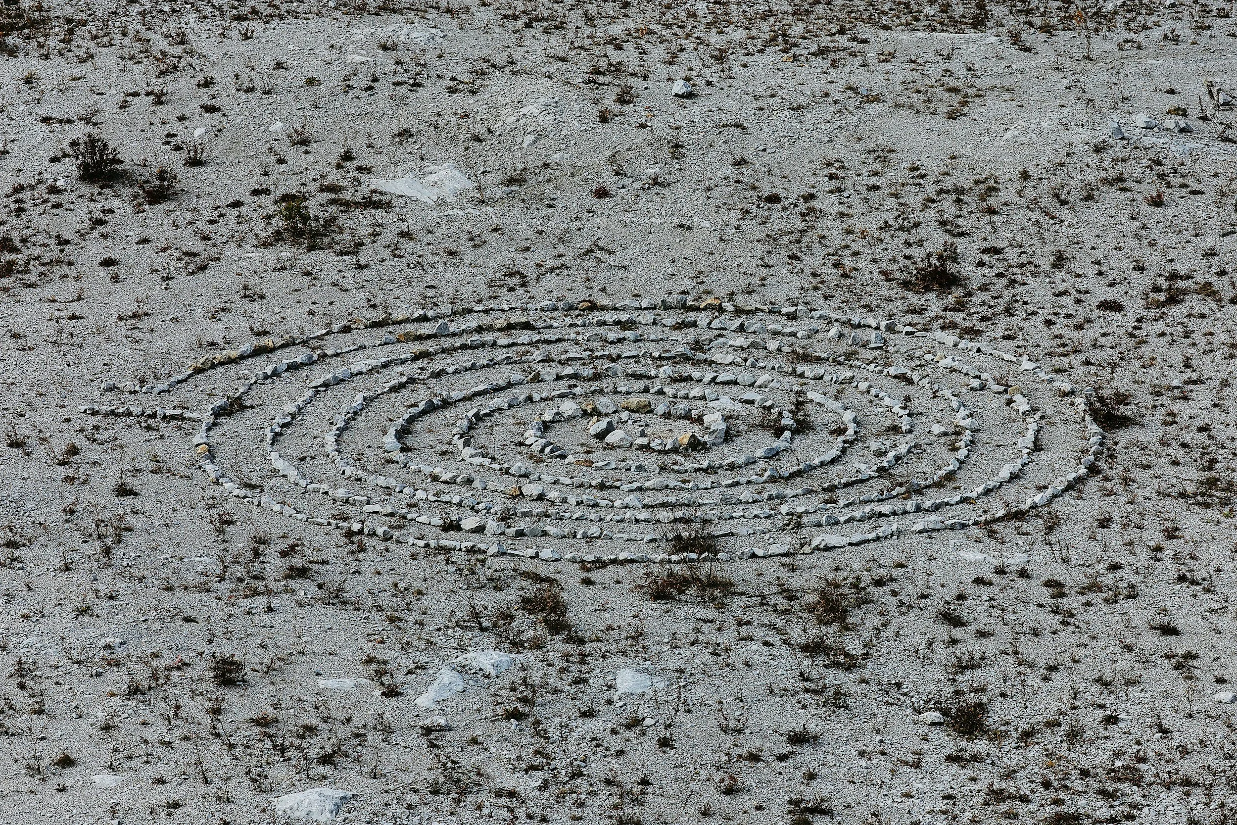Spiral pattern made of rocks on sandy, sparse desert terrain with small bushes.