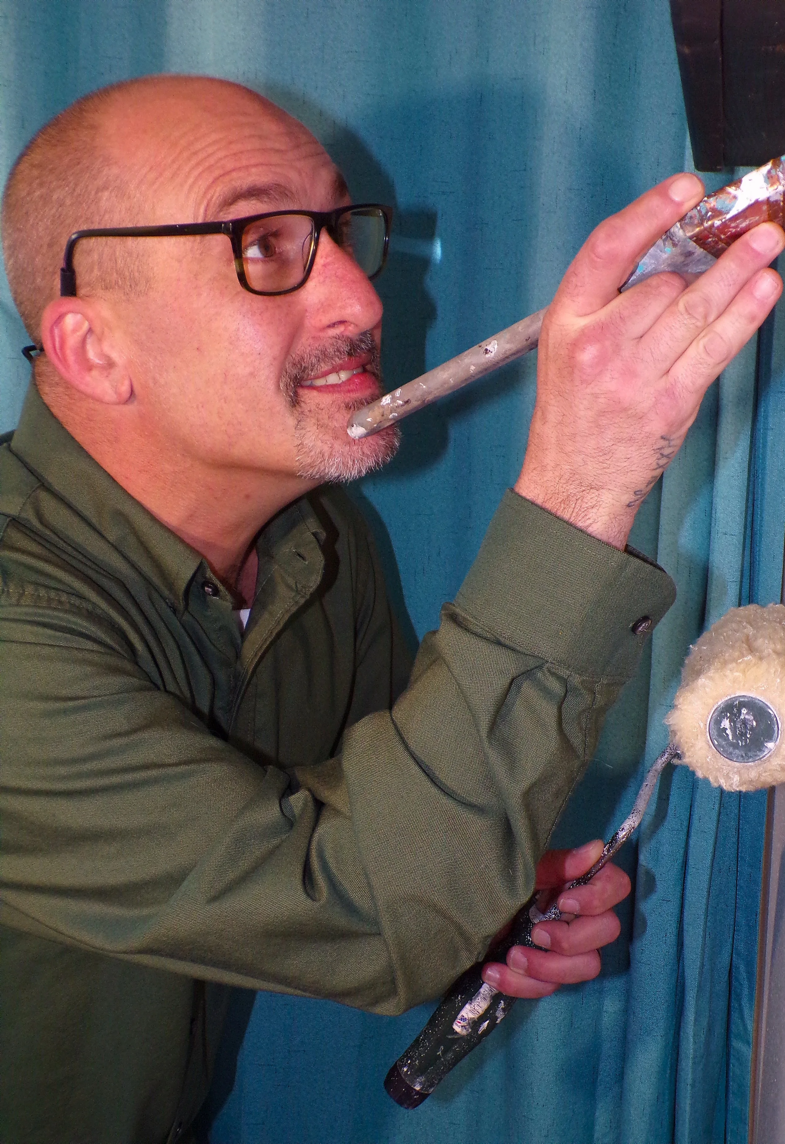 Man wearing glasses, painting a wall with a paint roller.