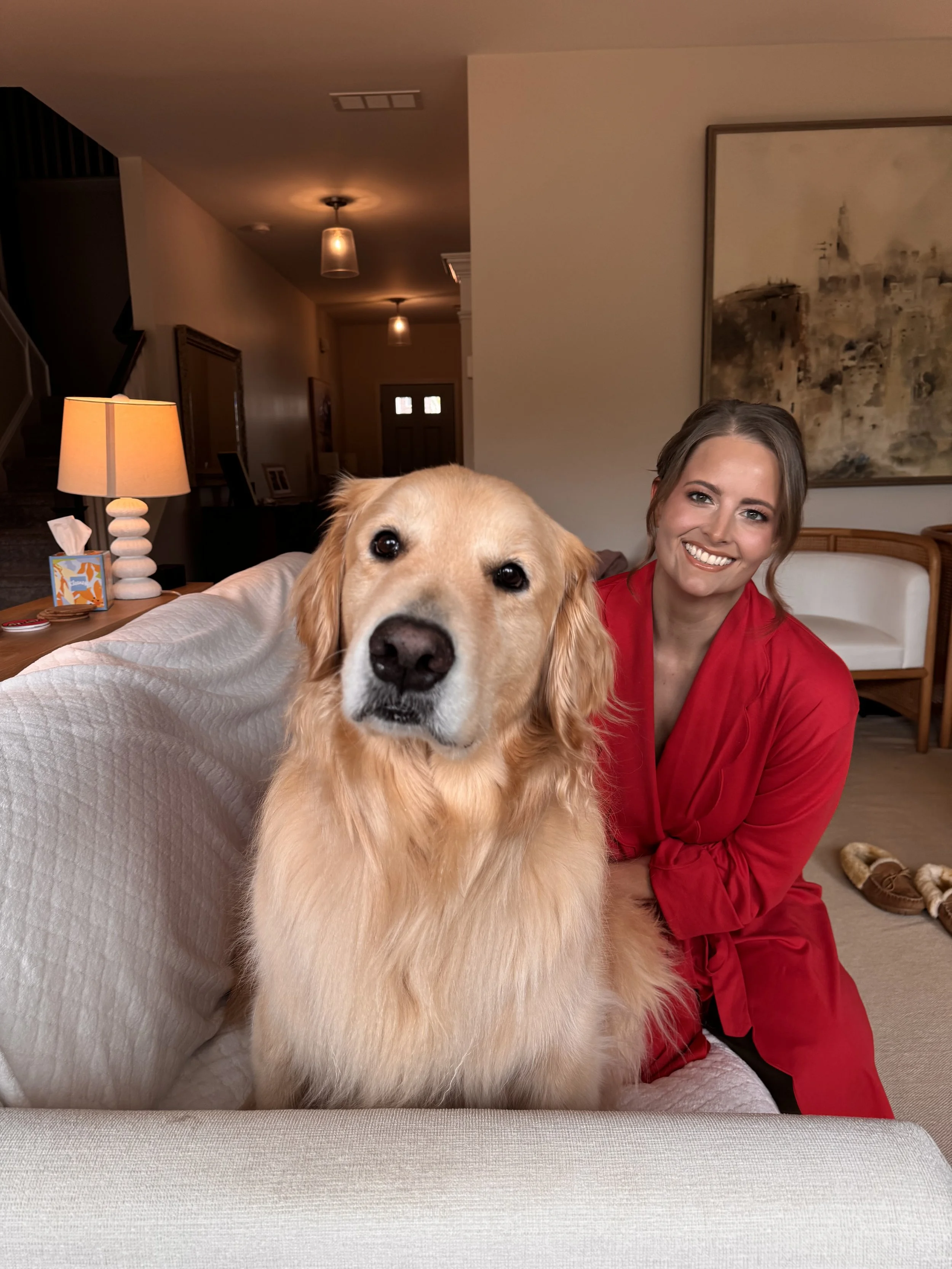 Melissa is with her golden retriever, Riley, sitting on a couch in a living room. She took a break from getting ready for the Woodstock Arts Gala to take a photo with Riley.