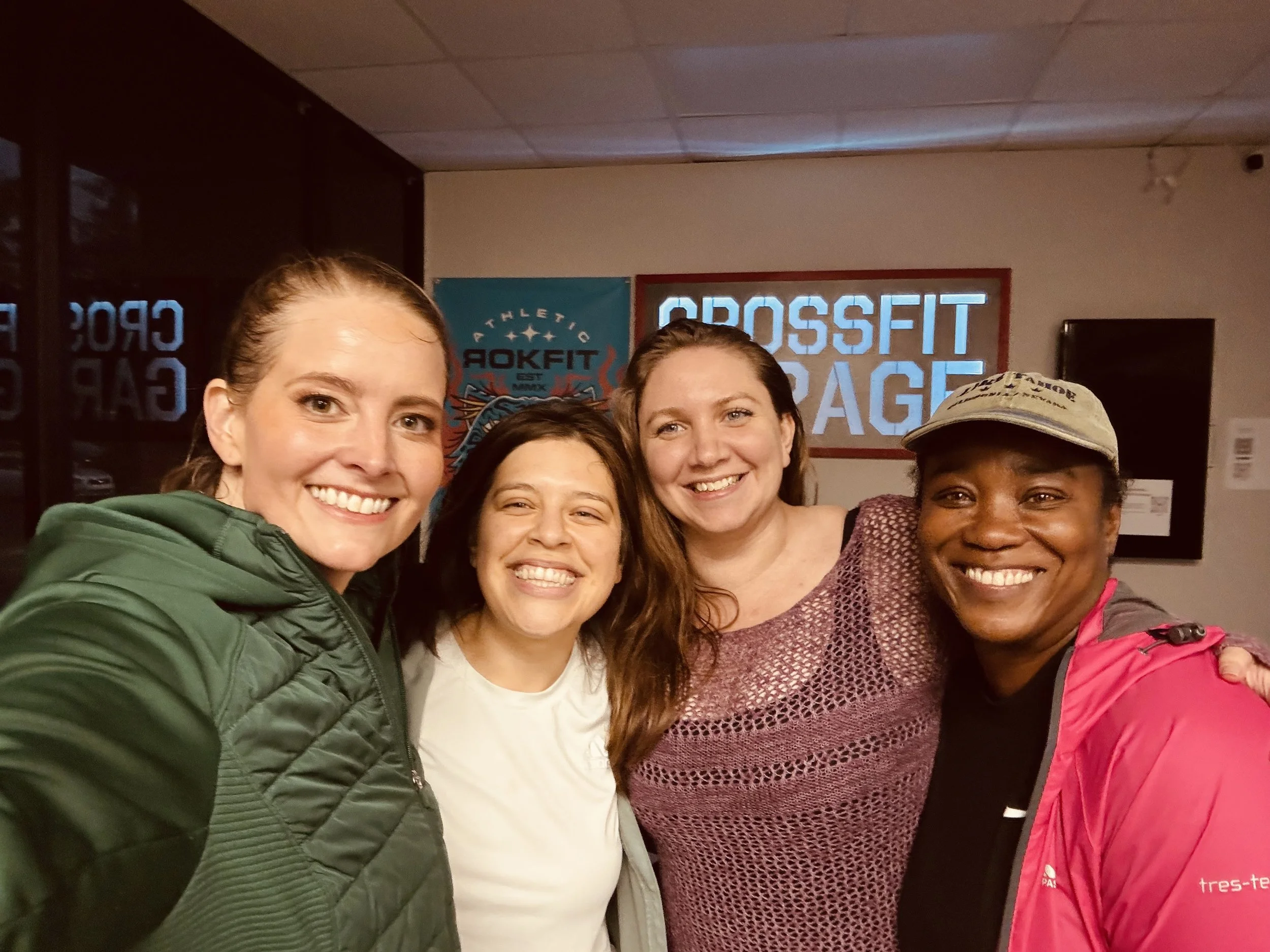Melissa with her gym friends, smiling and posing together in a gym, with a CrossFit Garage sign on the wall behind them.