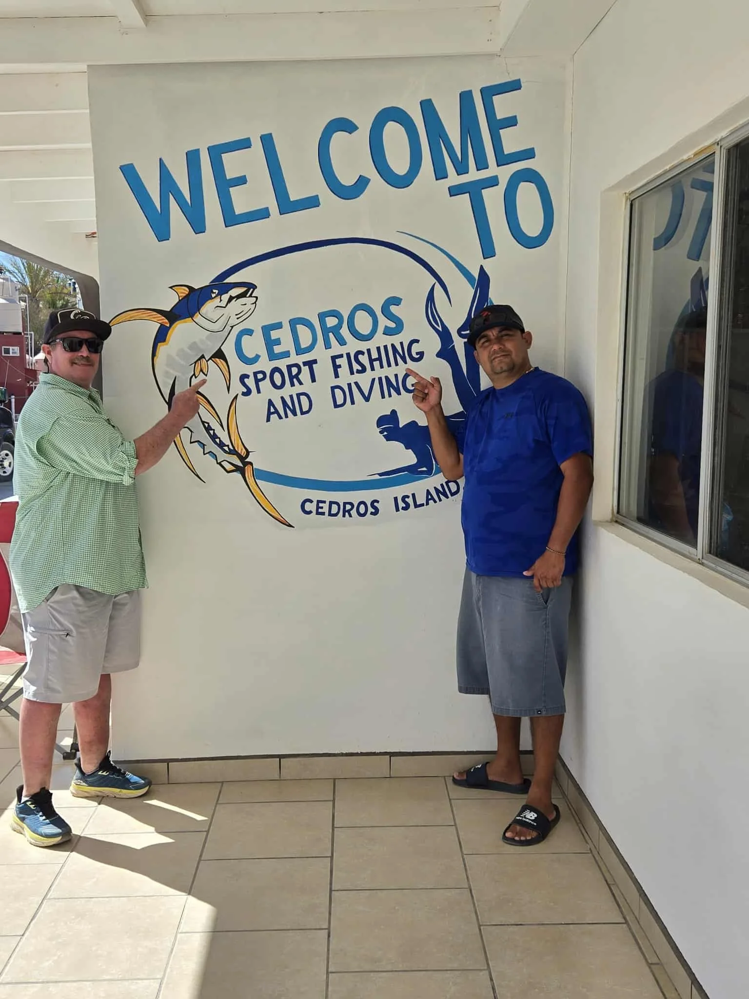 Guests standing by the Cedros Sport Fishing & Diving welcome sign on Cedros Island.