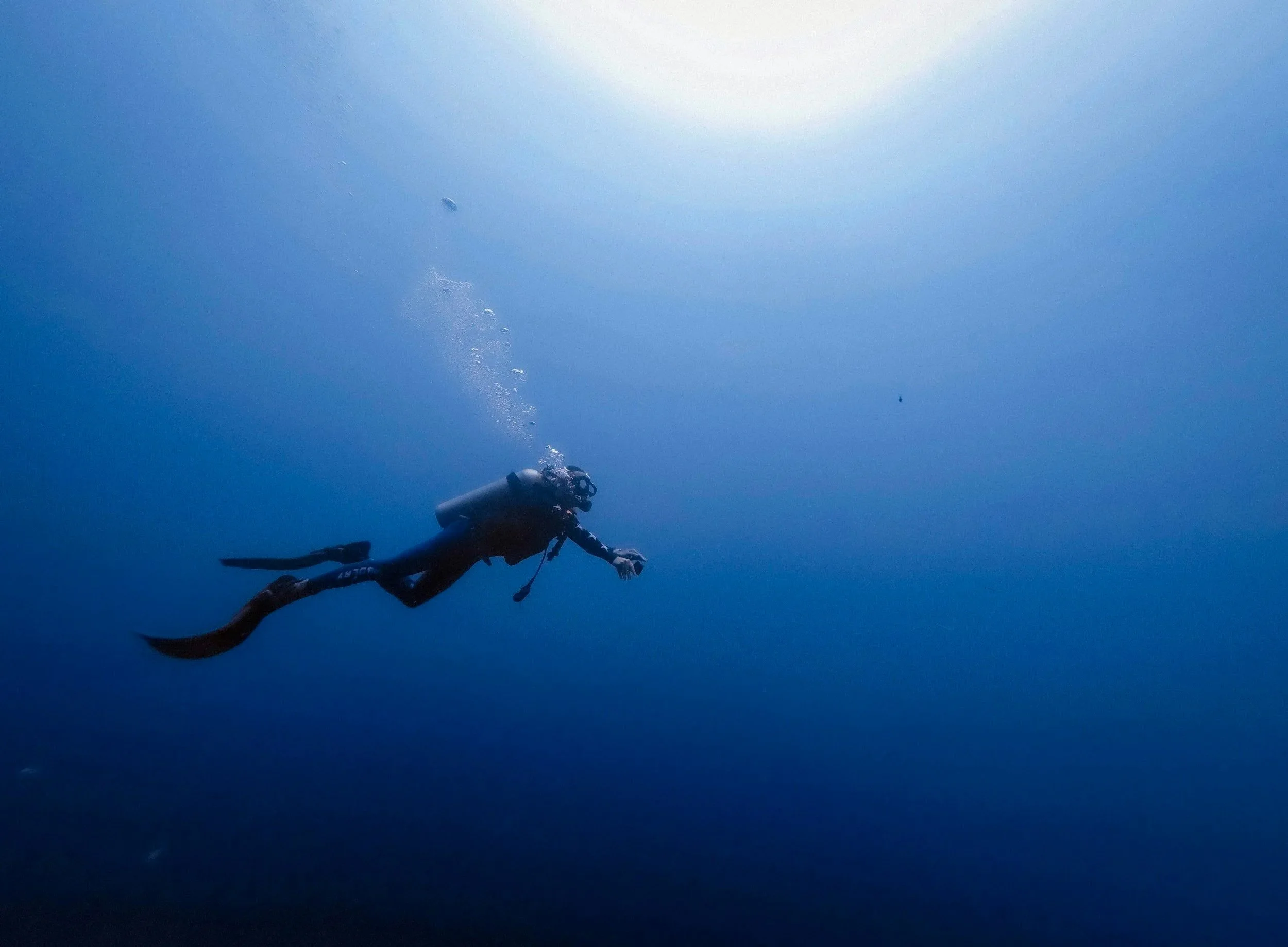 A scuba diver swimming underwater with the sun shining from above in the clear blue ocean.