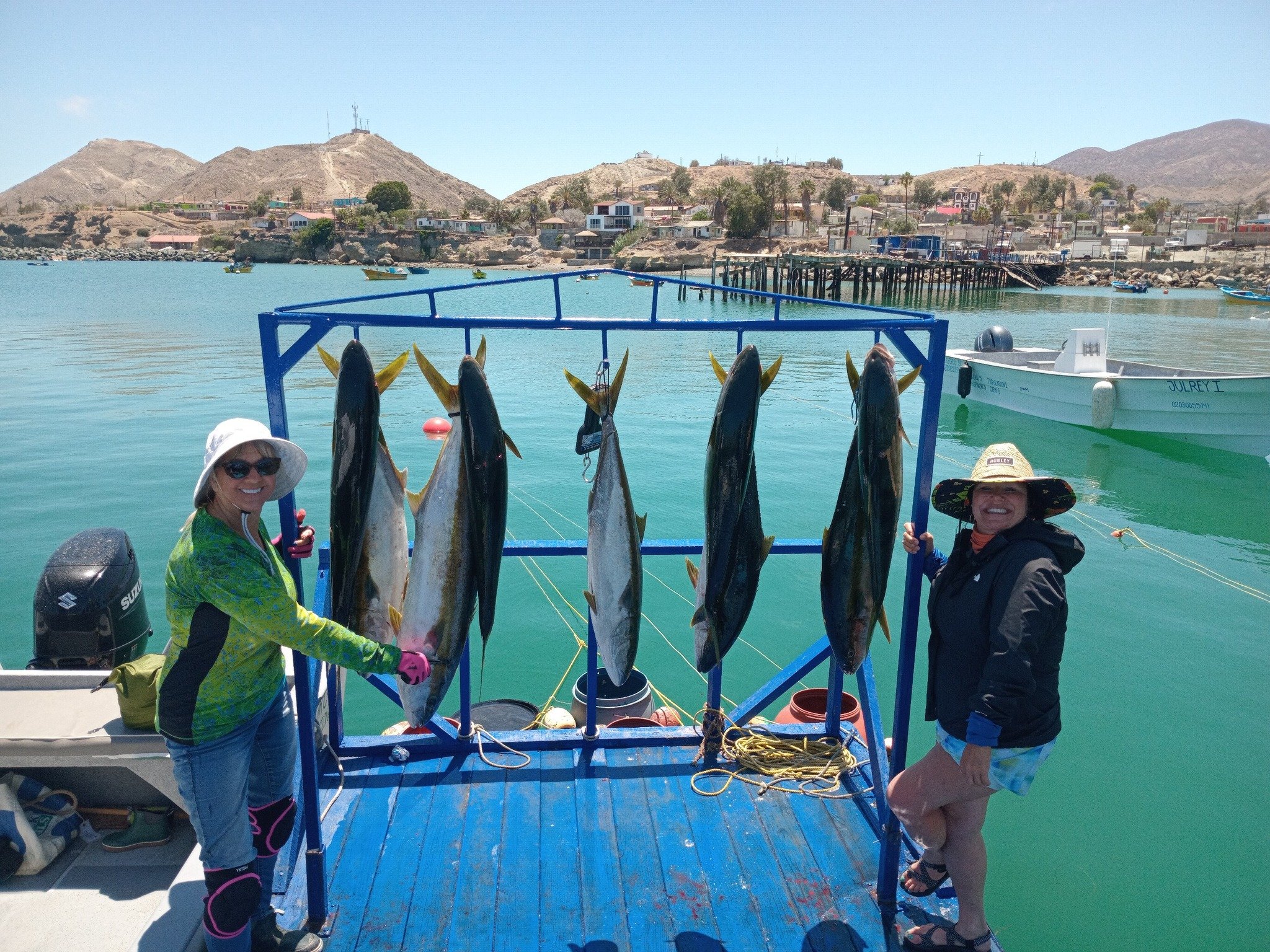 Two women standing on a boat holding large fish caught from the water, on their cedros fishing and diving trip.