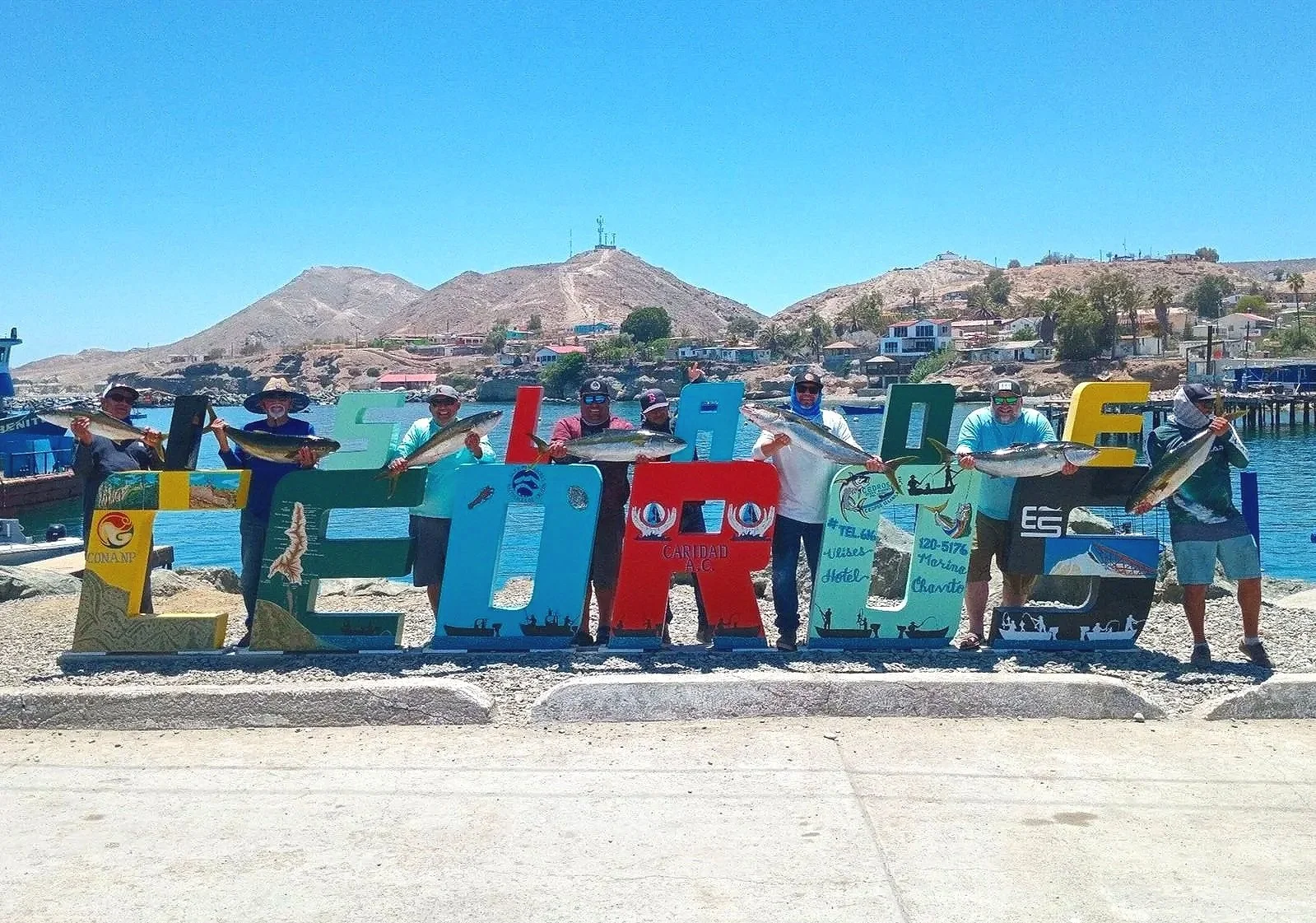 Group posing with their catch behind the colorful Cedros waterfront sign.