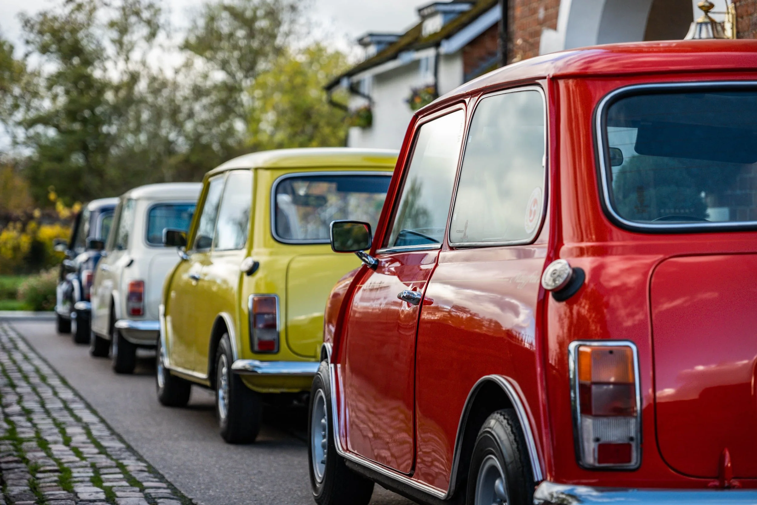 Line of vintage cars parked along a street in various colors including red, yellow, and white