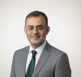 Professional portrait of a man with glasses, wearing a gray suit, white shirt, and green tie, against a plain white background.