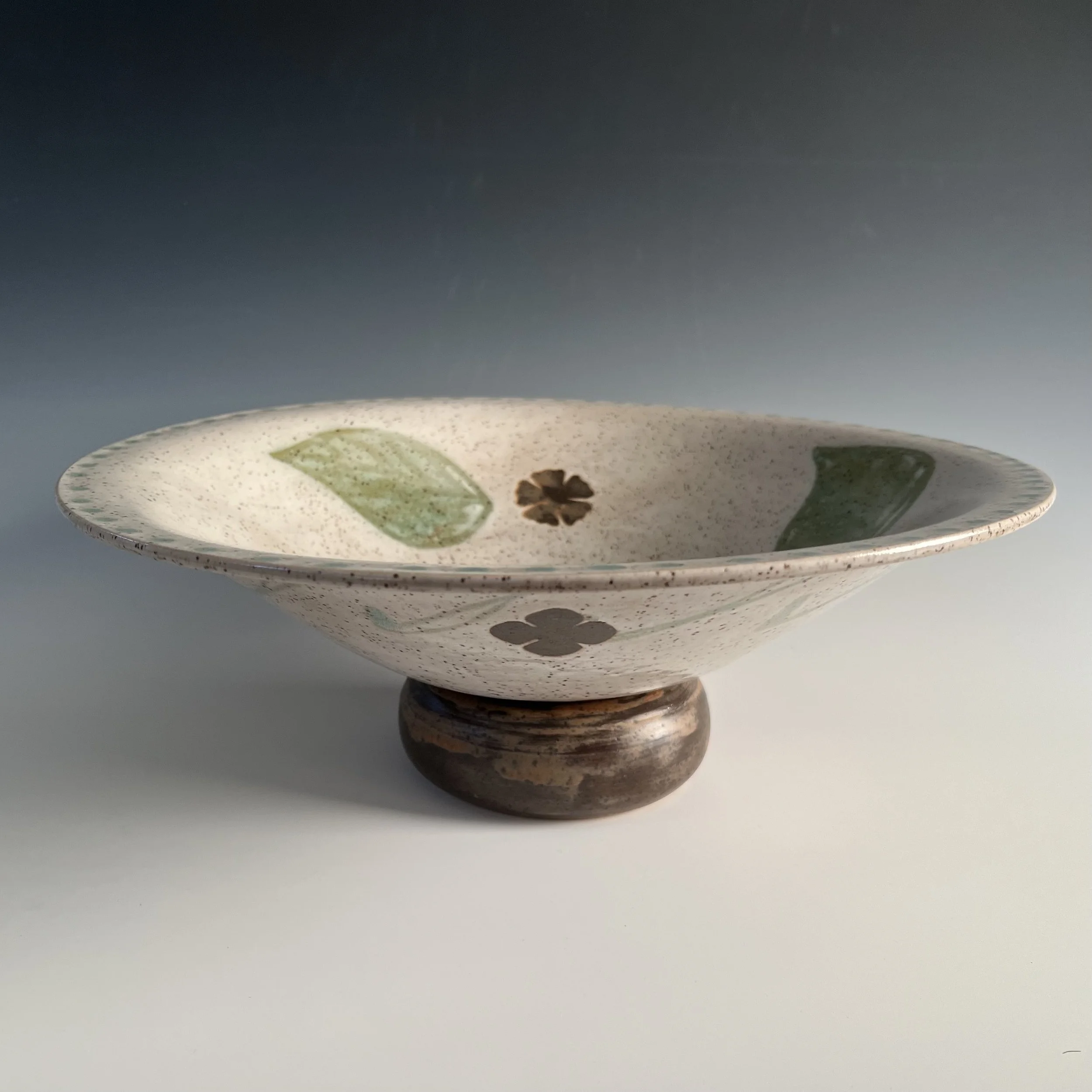 A large, flared bowl on round exaggerated foot with leaf and flower design. Stoneware clay thrown and decorated by me.