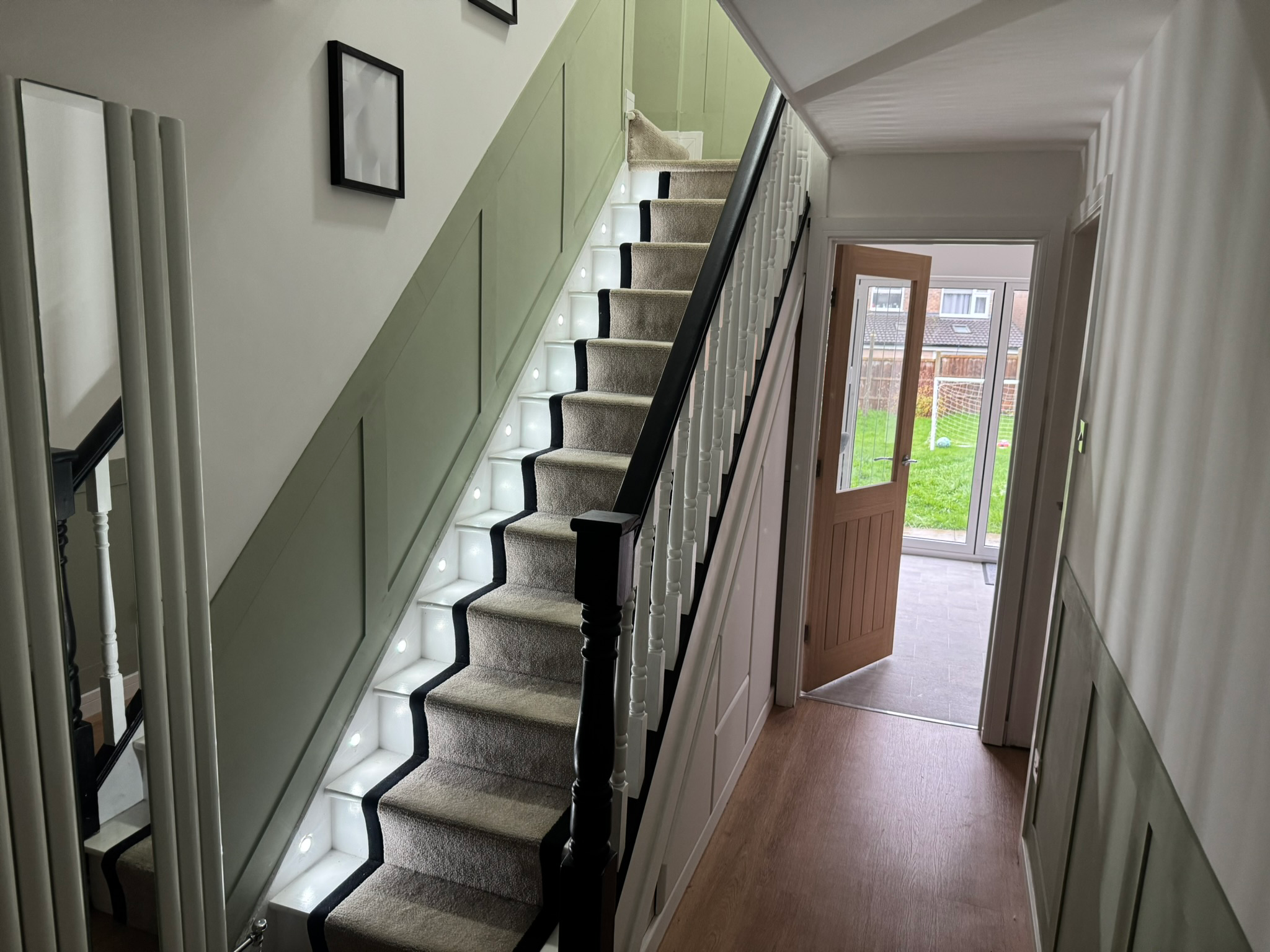 Interior view of a house showing a staircase with carpeted steps and built-in lighting, a door leading outside, and a view of a backyard with a soccer goal.