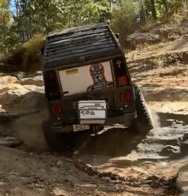A black off-road vehicle navigating rocky terrain in a wooded area.
