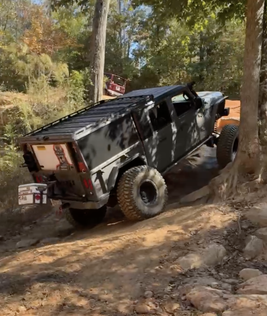 A black SUV with off-road tires navigating a steep, rocky trail in a forest.