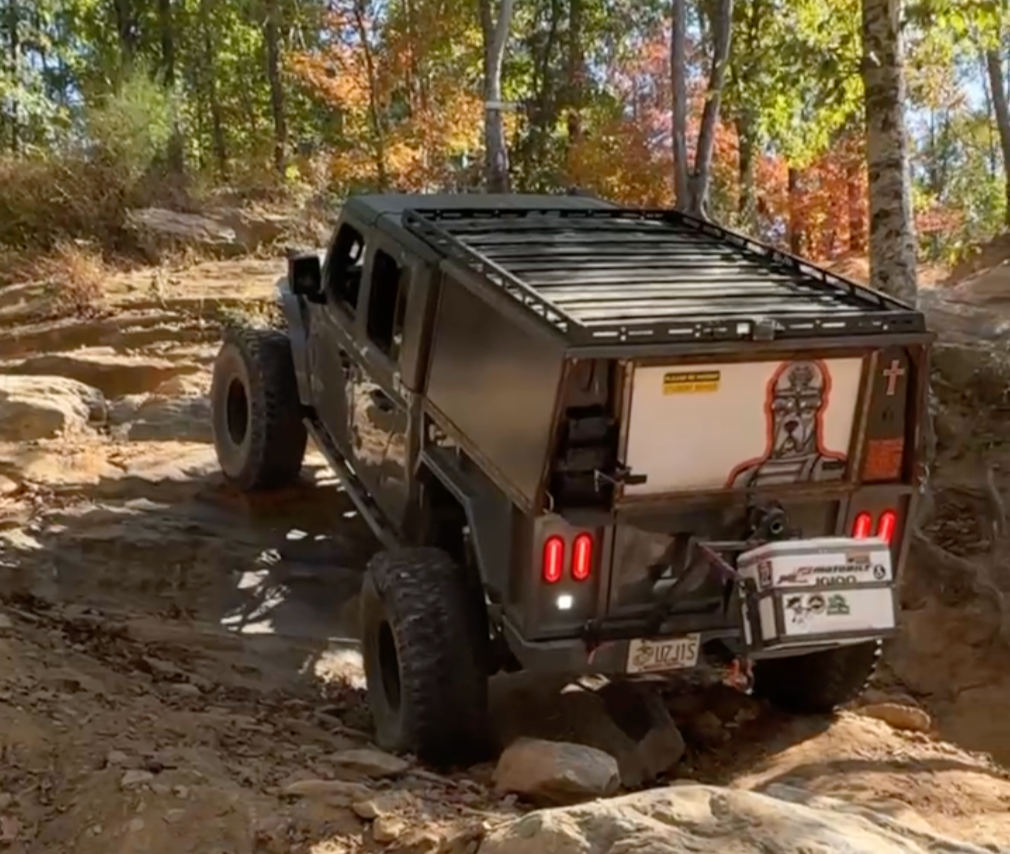 An off-road vehicle climbing a dirt trail with rocks in a wooded area with colorful fall foliage.