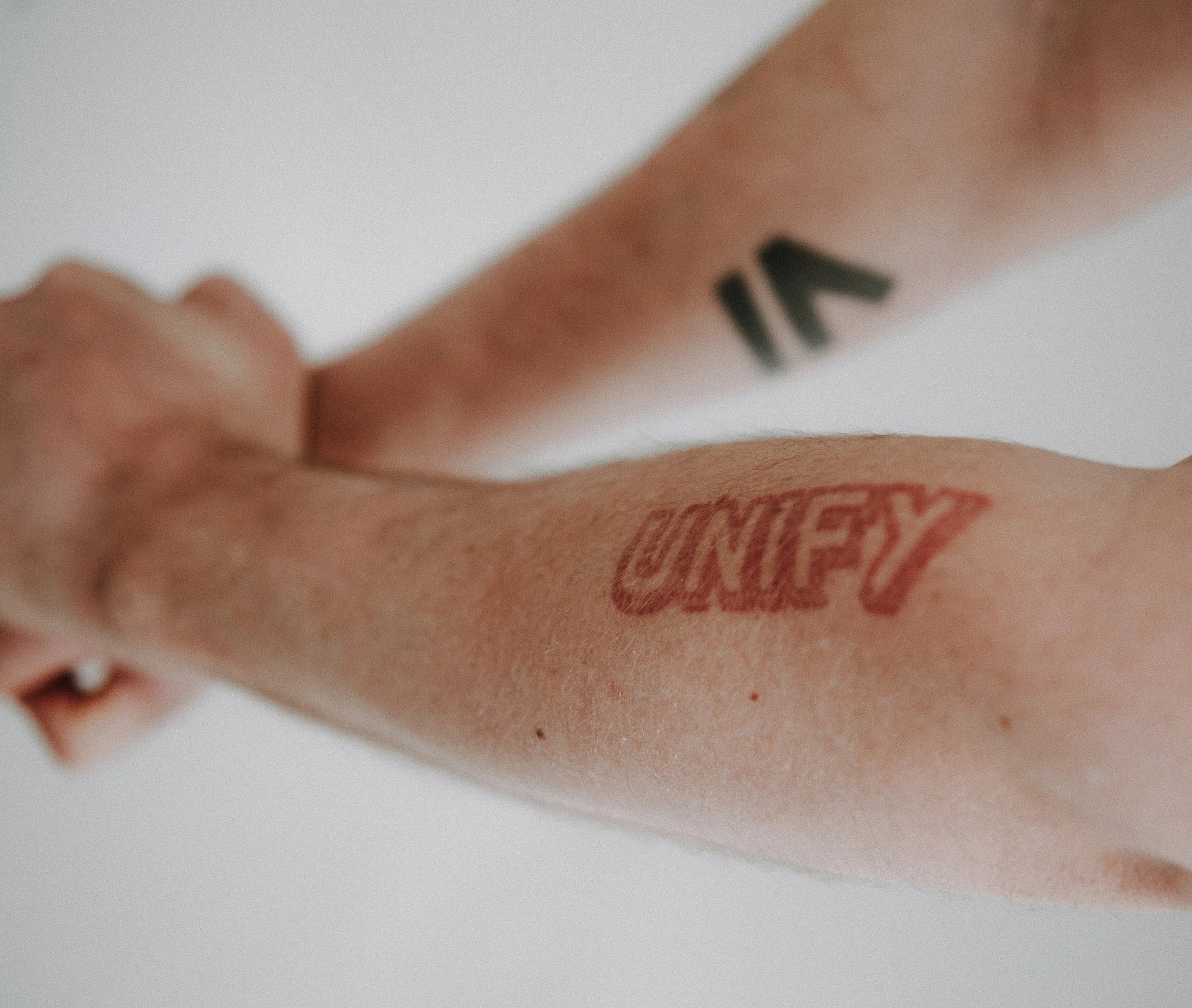 Nahaufnahme eines Arm Tattoos im Hintergrund eine weiße Oberfläche. Auf dem Arm ist tattoowiert: Unity was frei übersetzt verbinden heißt. Michael Schwarz, der Gestaltungscoach aus Bayreuth hat mehrere Tattoowierungen.