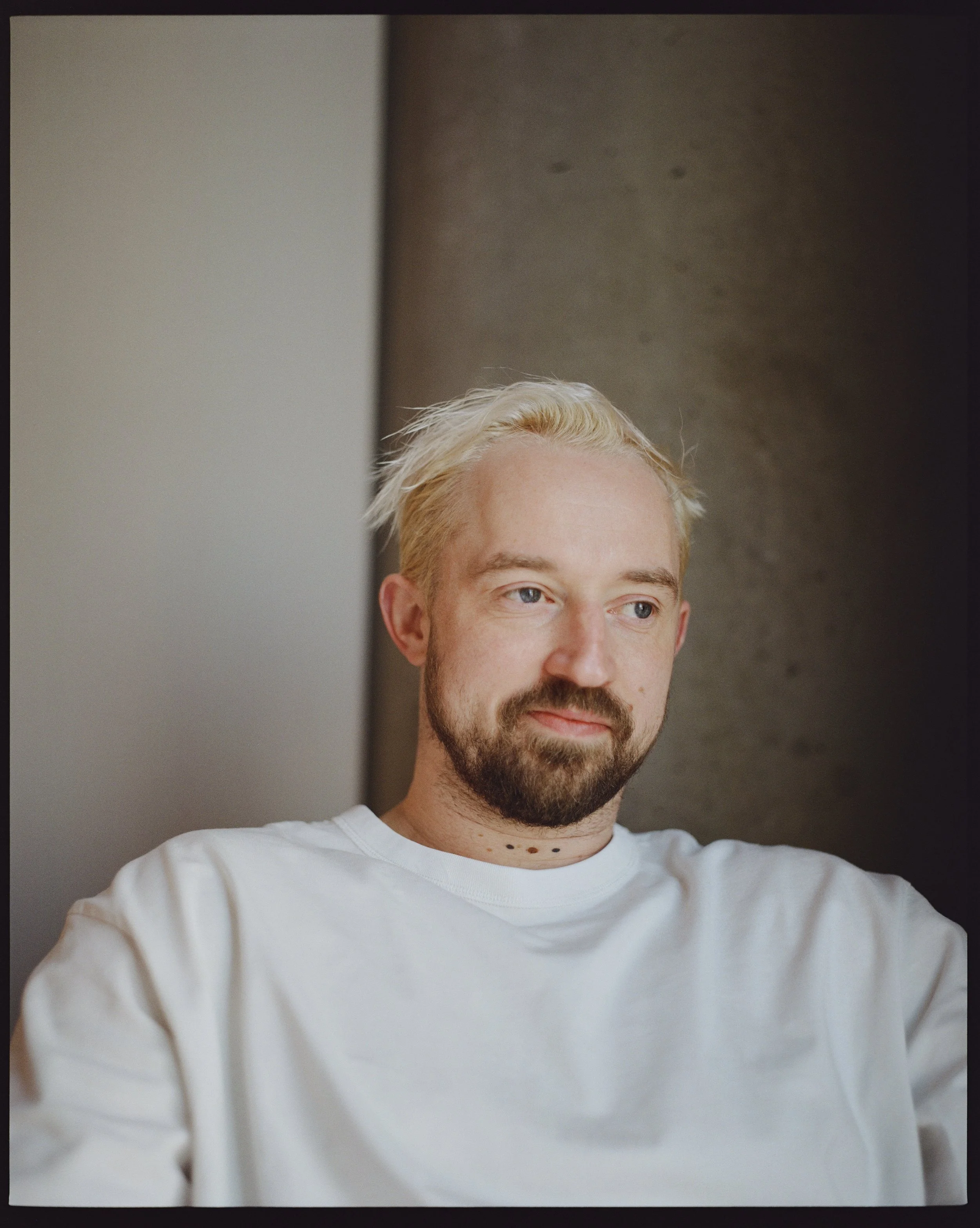 Nahaufnahme von Michael Schwarz mit blondem Haar, Vollbart und blauen Augen, der ein weißes T-Shirt trägt, vor neutralem Hintergrund.