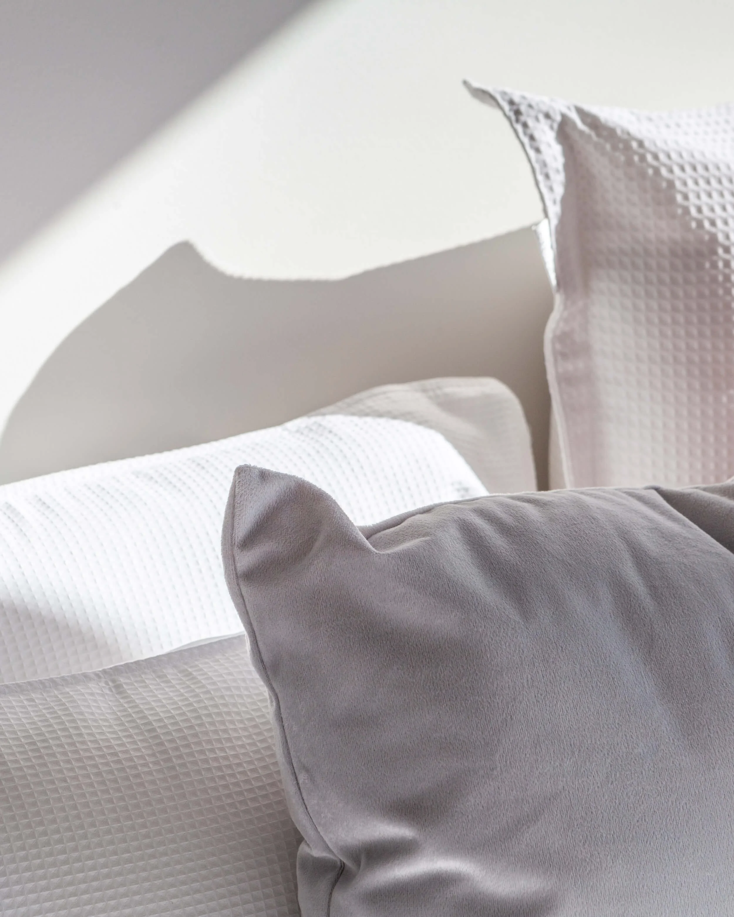 Close-up of decorative pillows on a bed with textured white and gray fabric, soft lighting, and a well-lit bedroom setting.