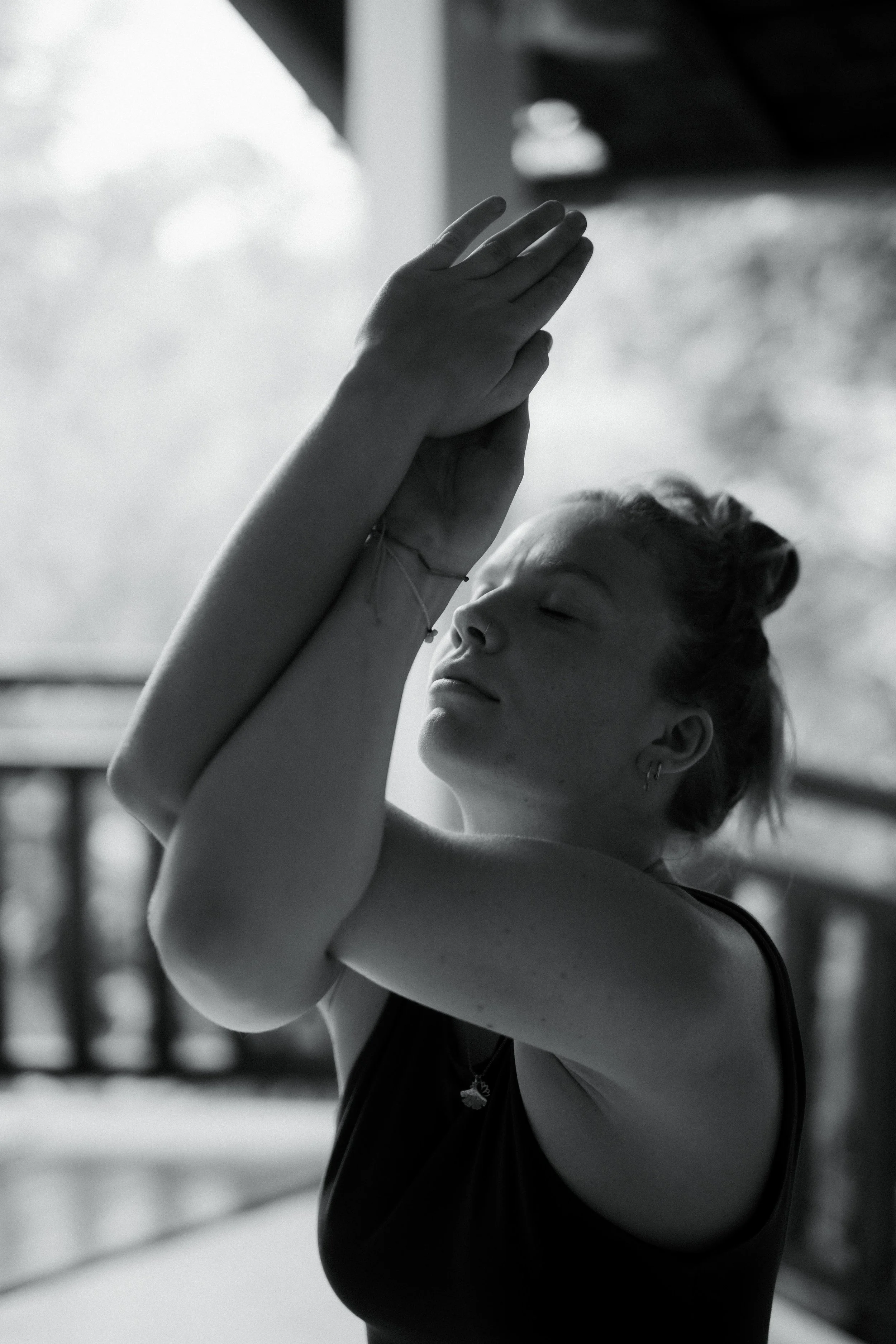 Young woman with closed eyes, touching her forehead with both hands, standing outdoors on a balcony with blurred natural background.