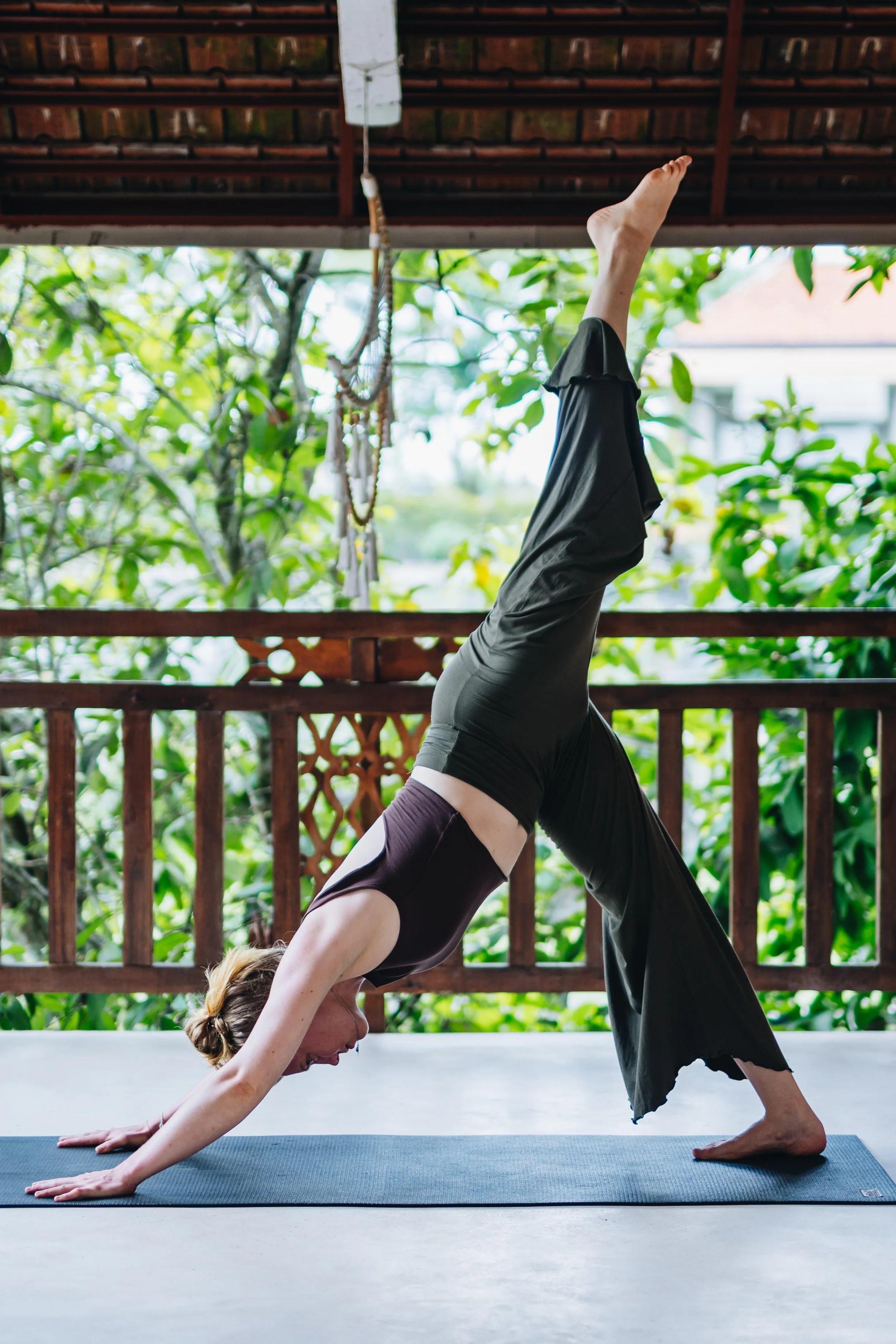 A woman practicing yoga outdoors on a mat, balancing in a downward dog position with one leg raised.