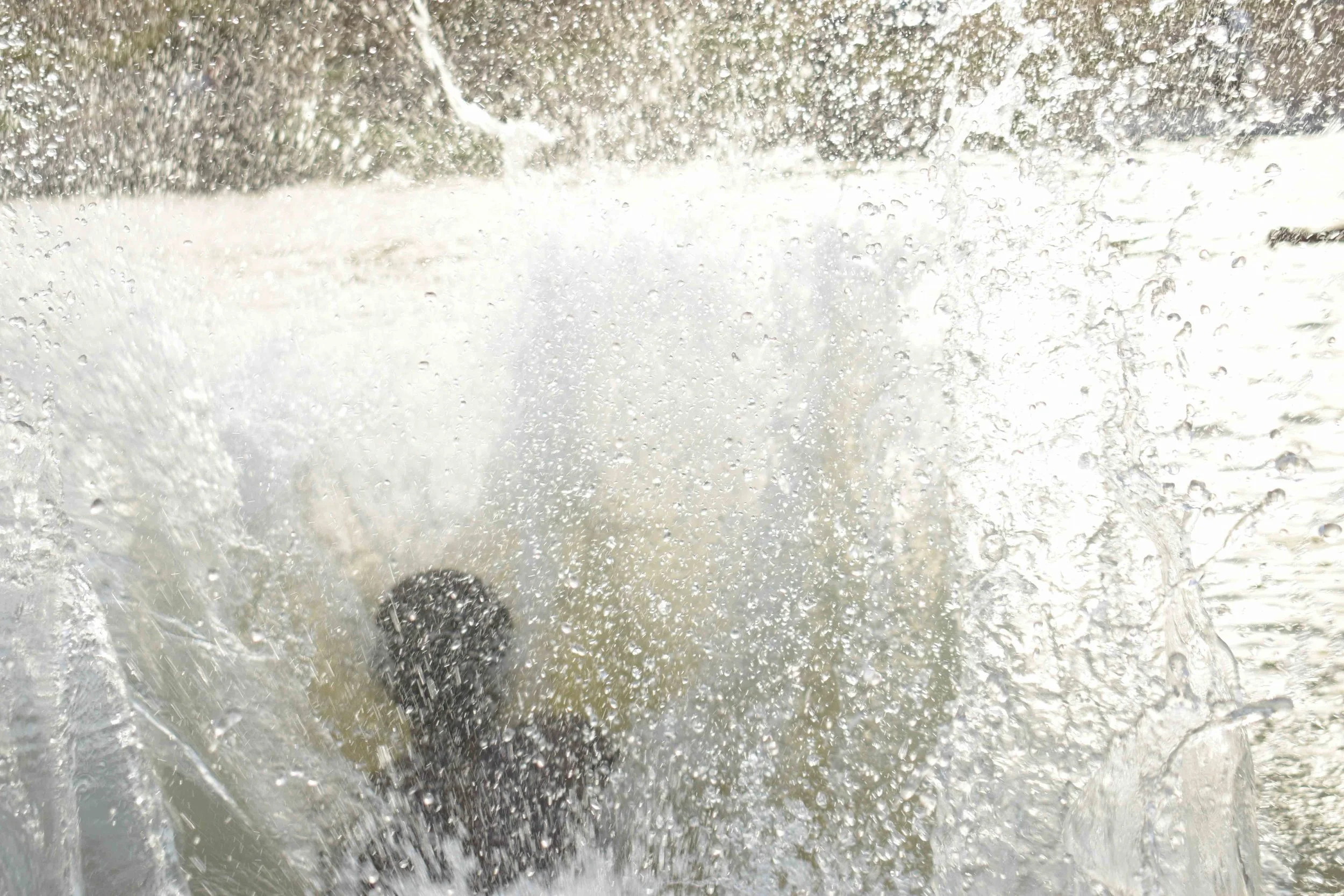View through a car windshield with water and rain droplets, showing a blurred scene outside.