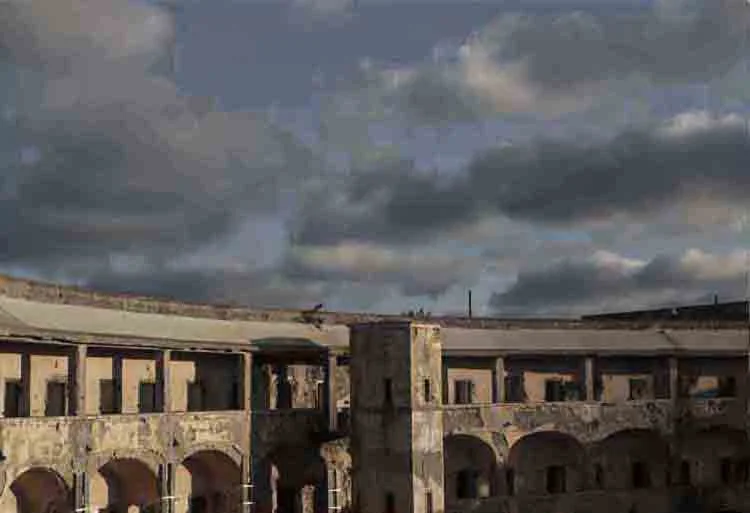 An old, abandoned stone building or fort with multiple arches and windows under a cloudy sky.
